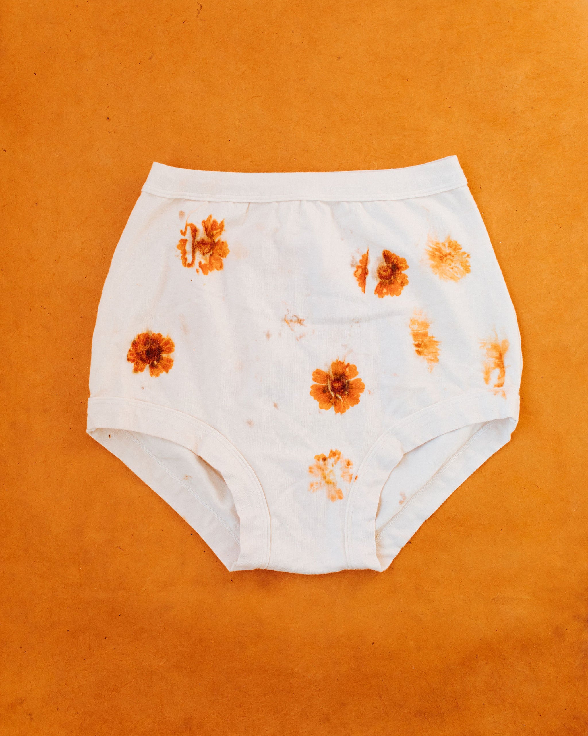 Flat lay on an orange surface of Thunderpants Sky Rise style underwear in the Limited Edition Flower Press Botanical Dye - flowers pressed on the underwear to create a print.