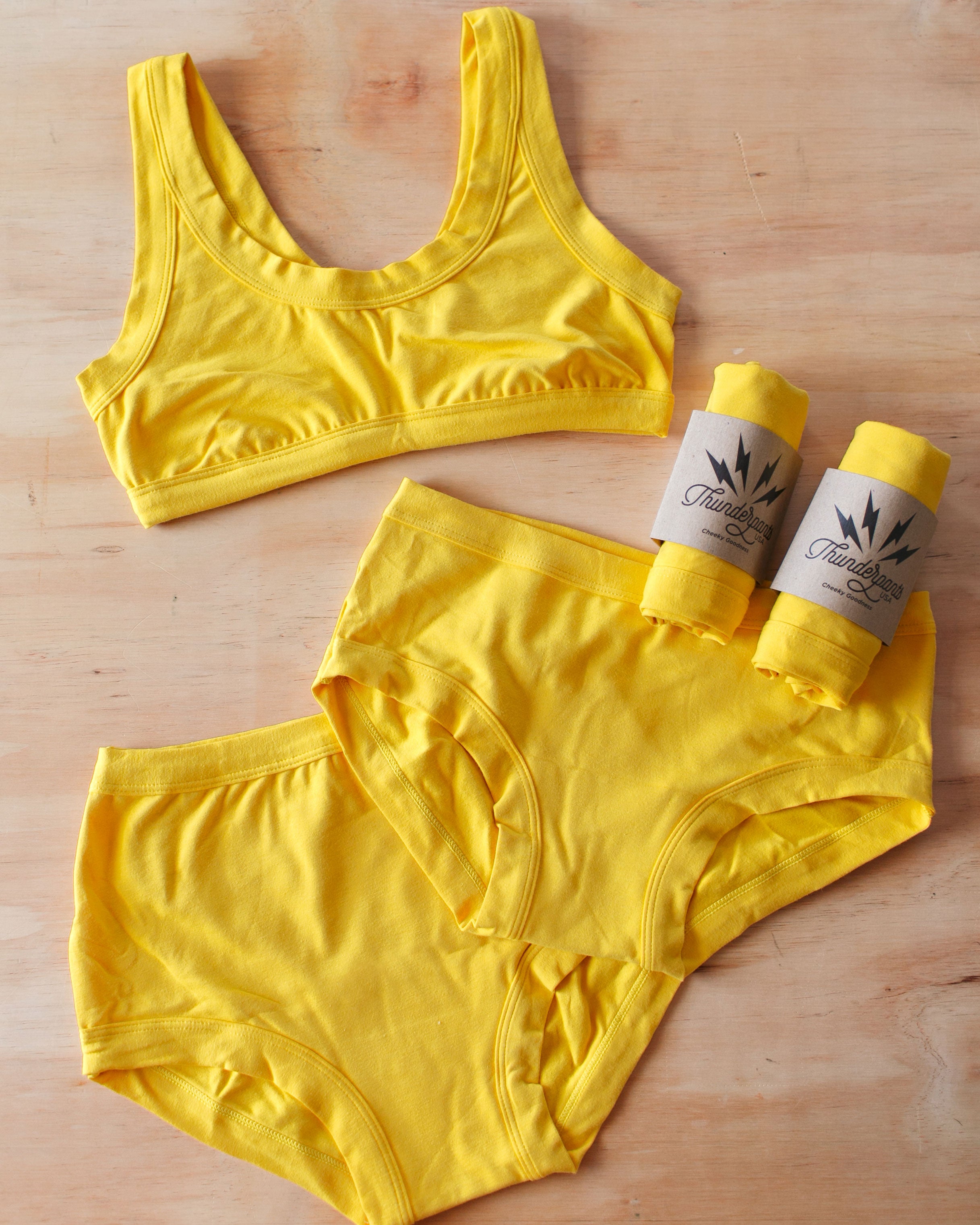 Flat lay of Thunderpants Organic Cotton Bralette, Hipster style and Original style underwear with packaged underwear in Golden Yellow color.