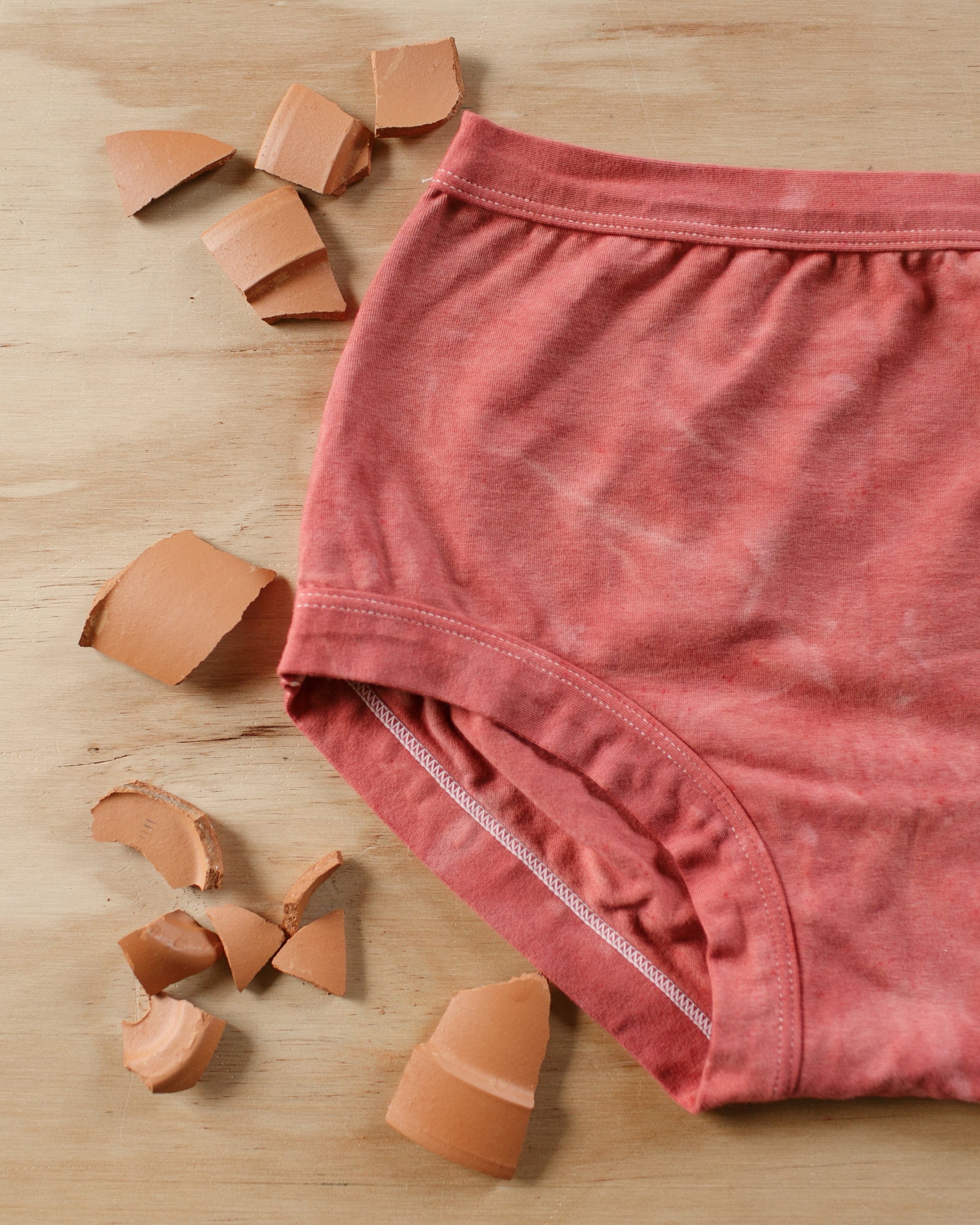 Flat lay of Thunderpants organic cotton Original underwear in hand dyed Terracotta color with broken terracotta around.