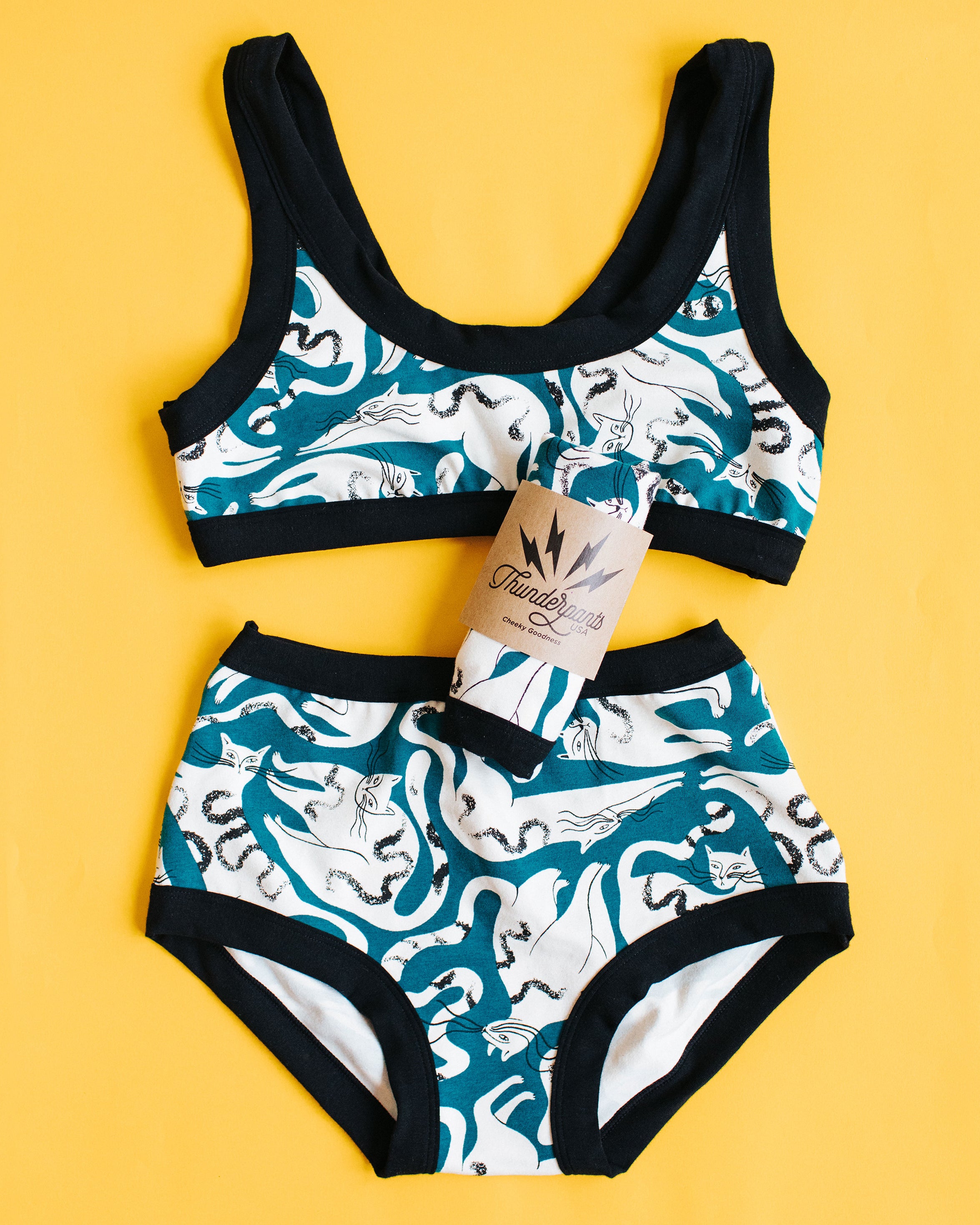 Flat lay on yellow background of Thunderpants Original style underwear and Bralette set in Hey Meow! print - green with white cats.