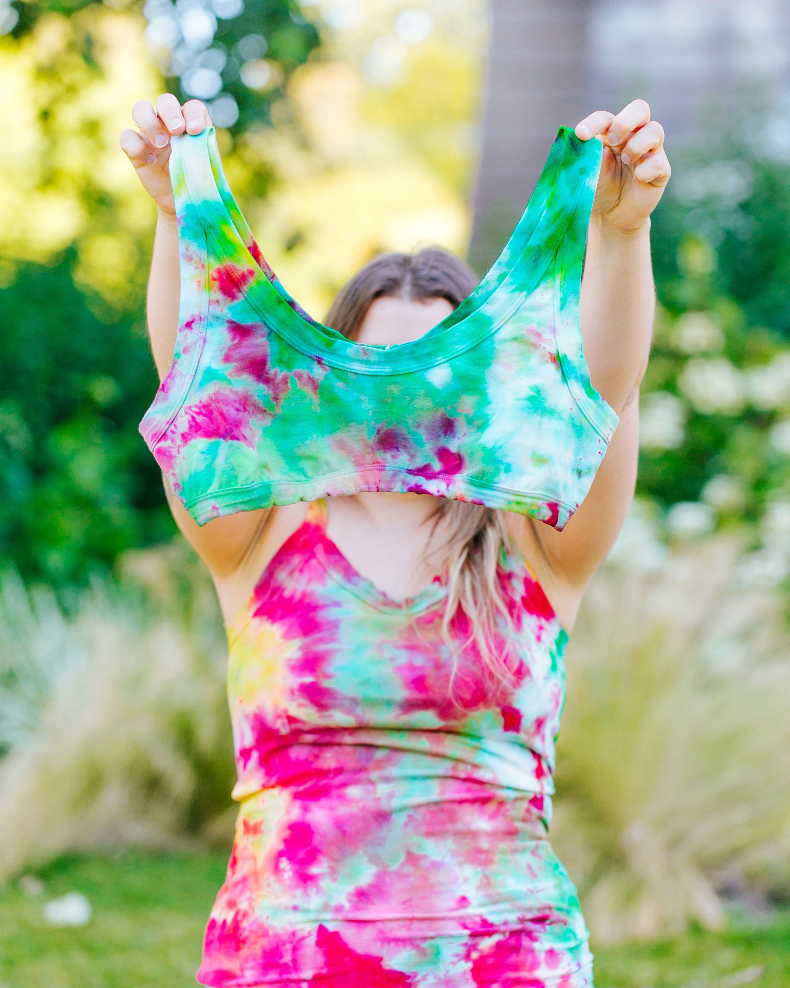 Model holding up an Ice Dyed Bralette with a mix of bright green and pink colors.