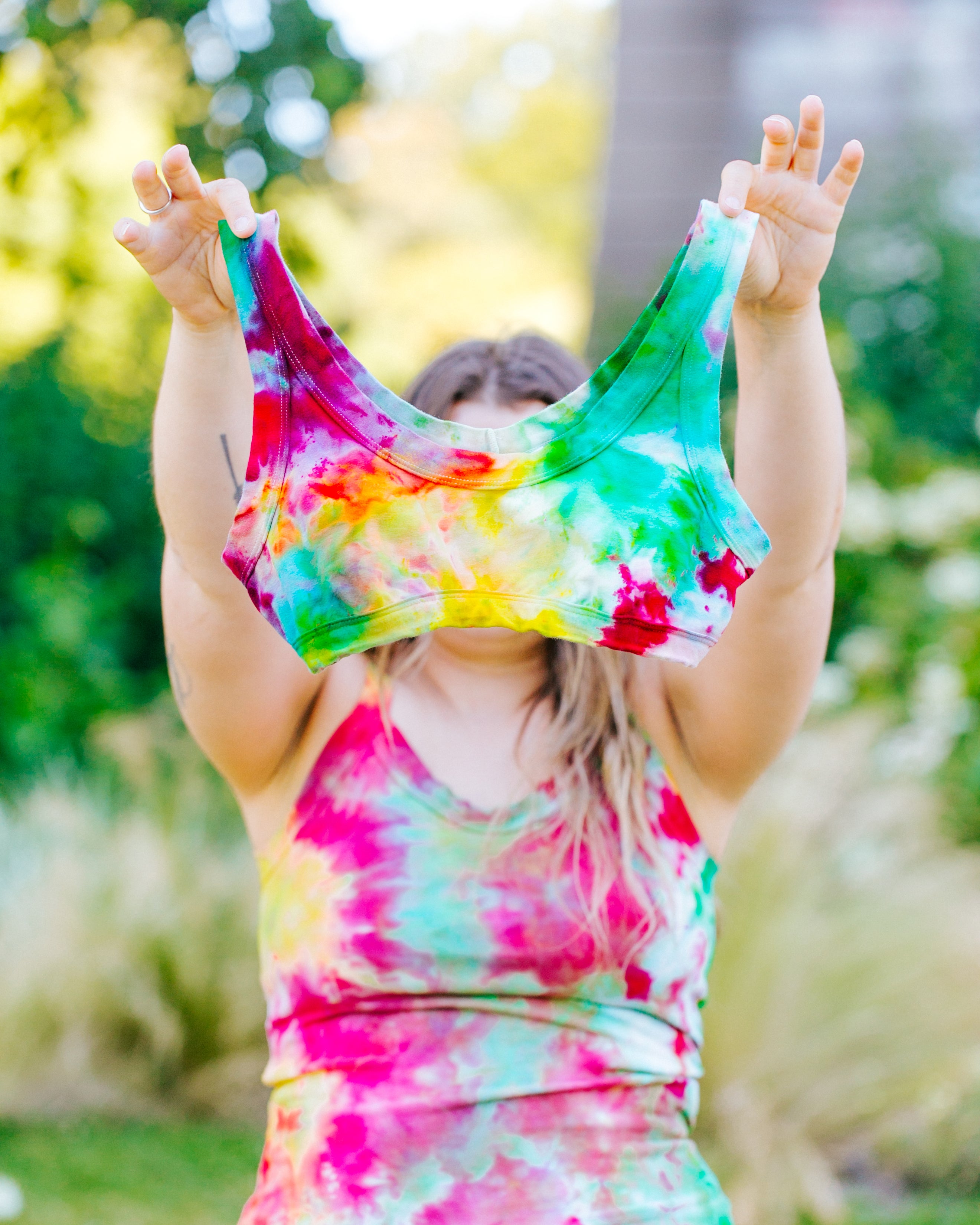 Model holding up an Ice Dye Bralette with a mix of bright yellow, pink, green, and blue colors.