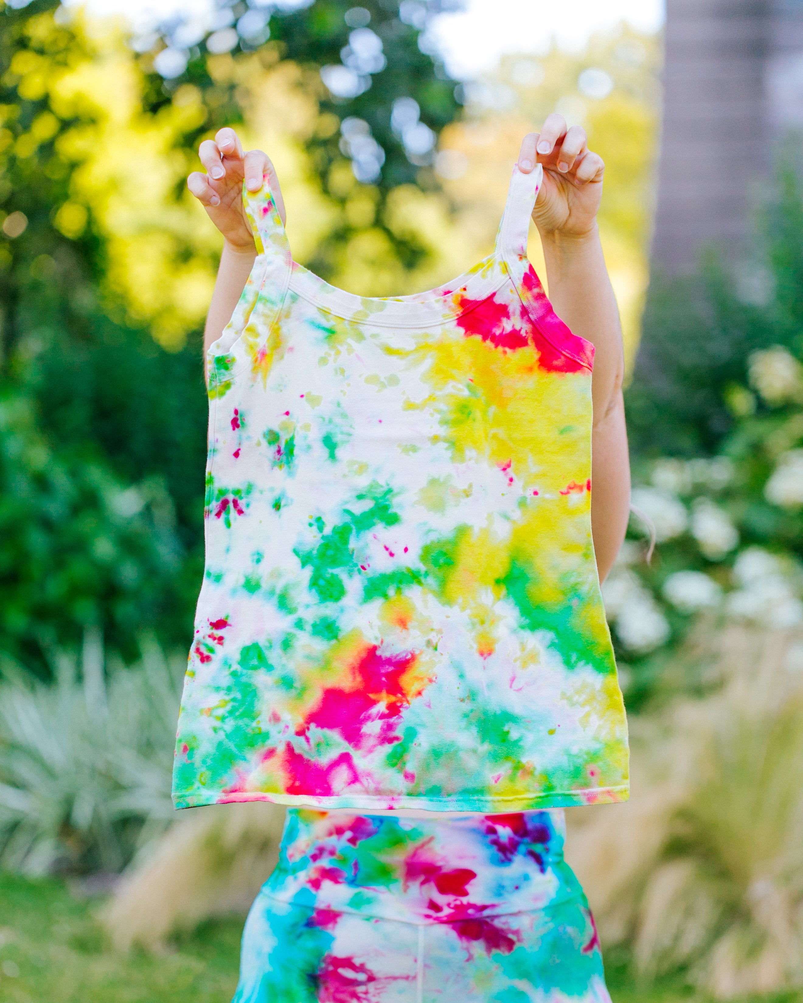 Model wearing Ice Dyed Bike Shorts holding up an Ice Dyed Camisole in a mix of green, pink, and yellow colors.