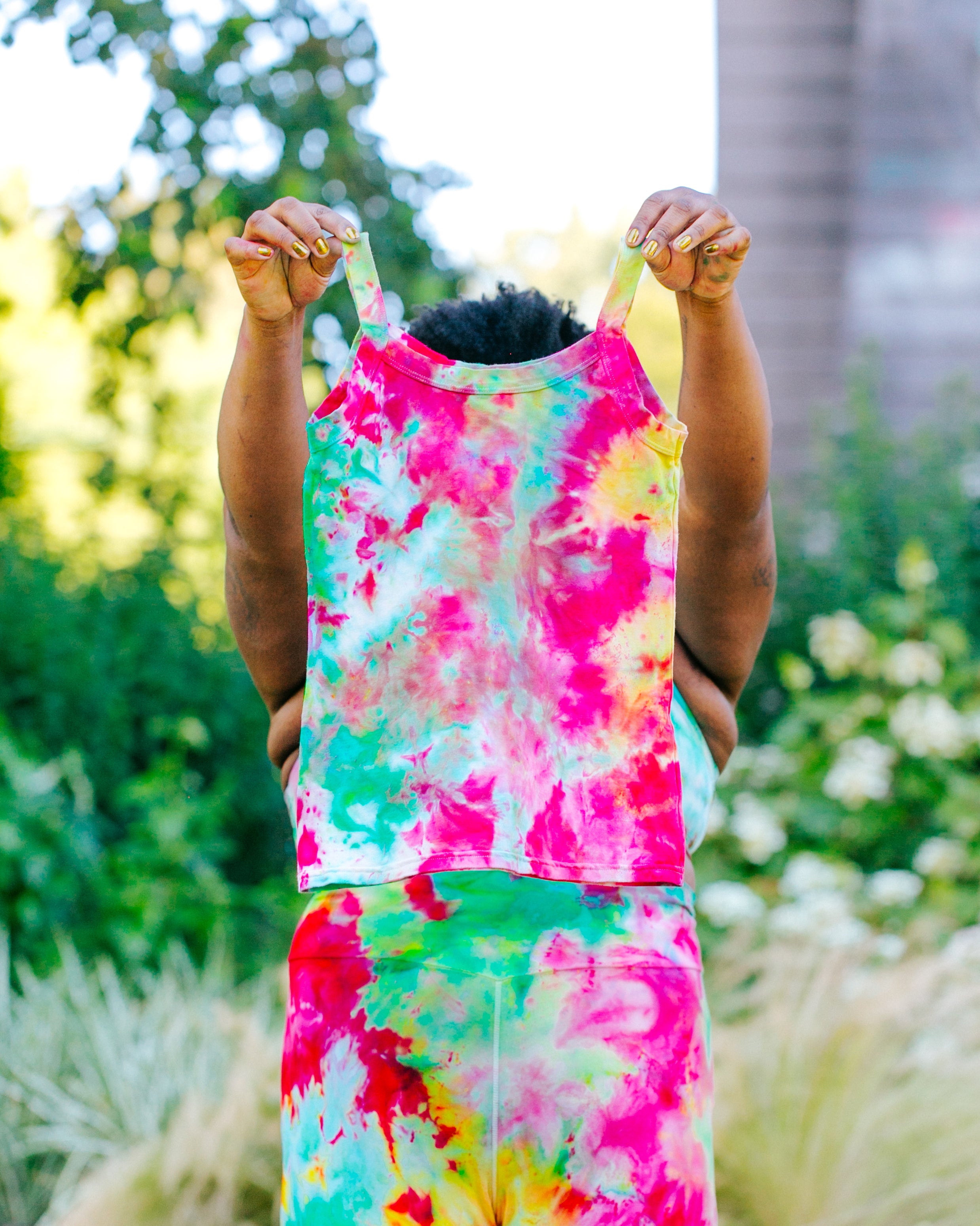 Model wearing Ice Dyed Bike Shorts holding up an Ice Dyed Camisole with a mix of bright pink, green, and yellow colors.
