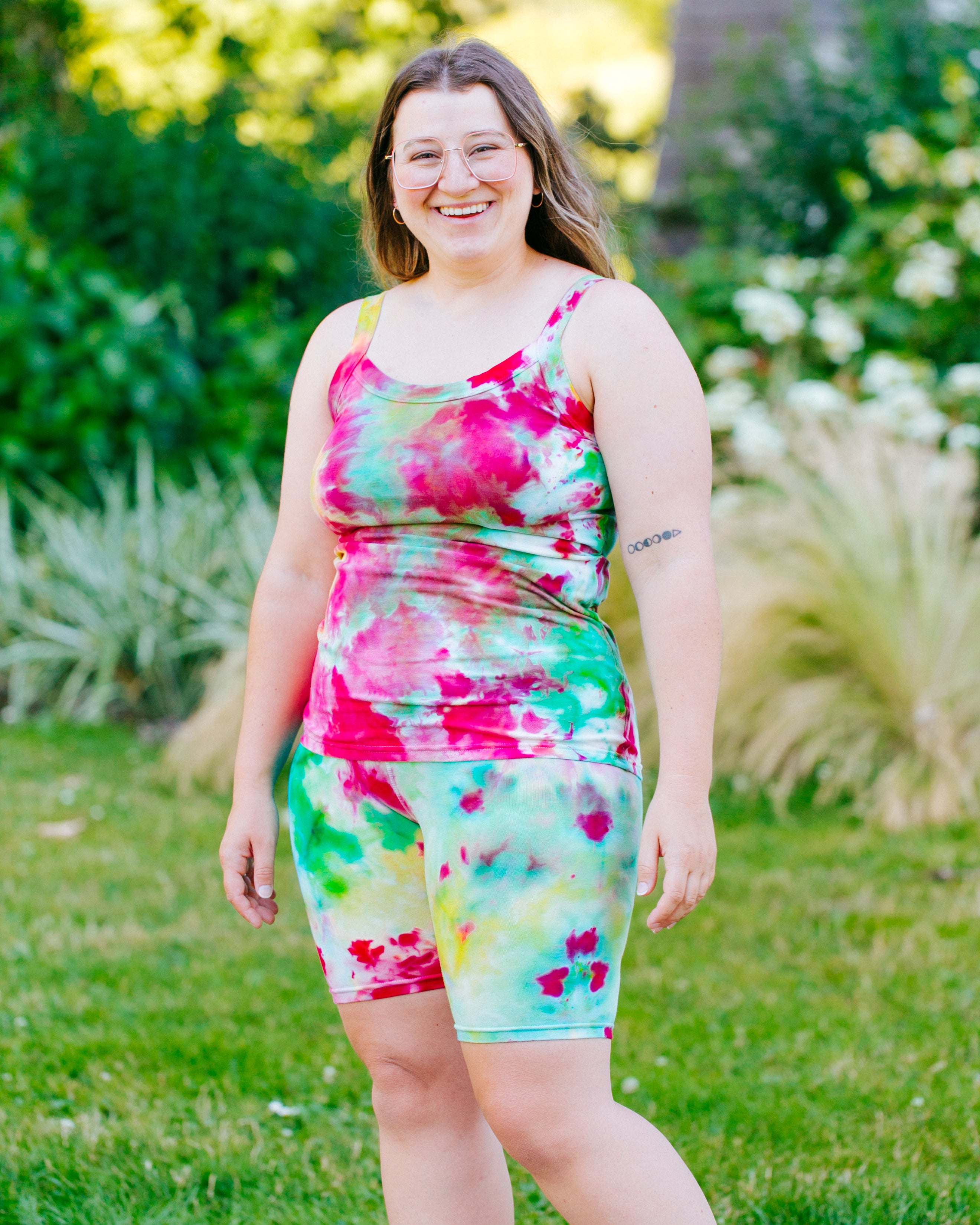 Model smiling and wearing Ice Dyed Camisole and Bike Shorts in a mix of bright green, pink, and yellow colors.