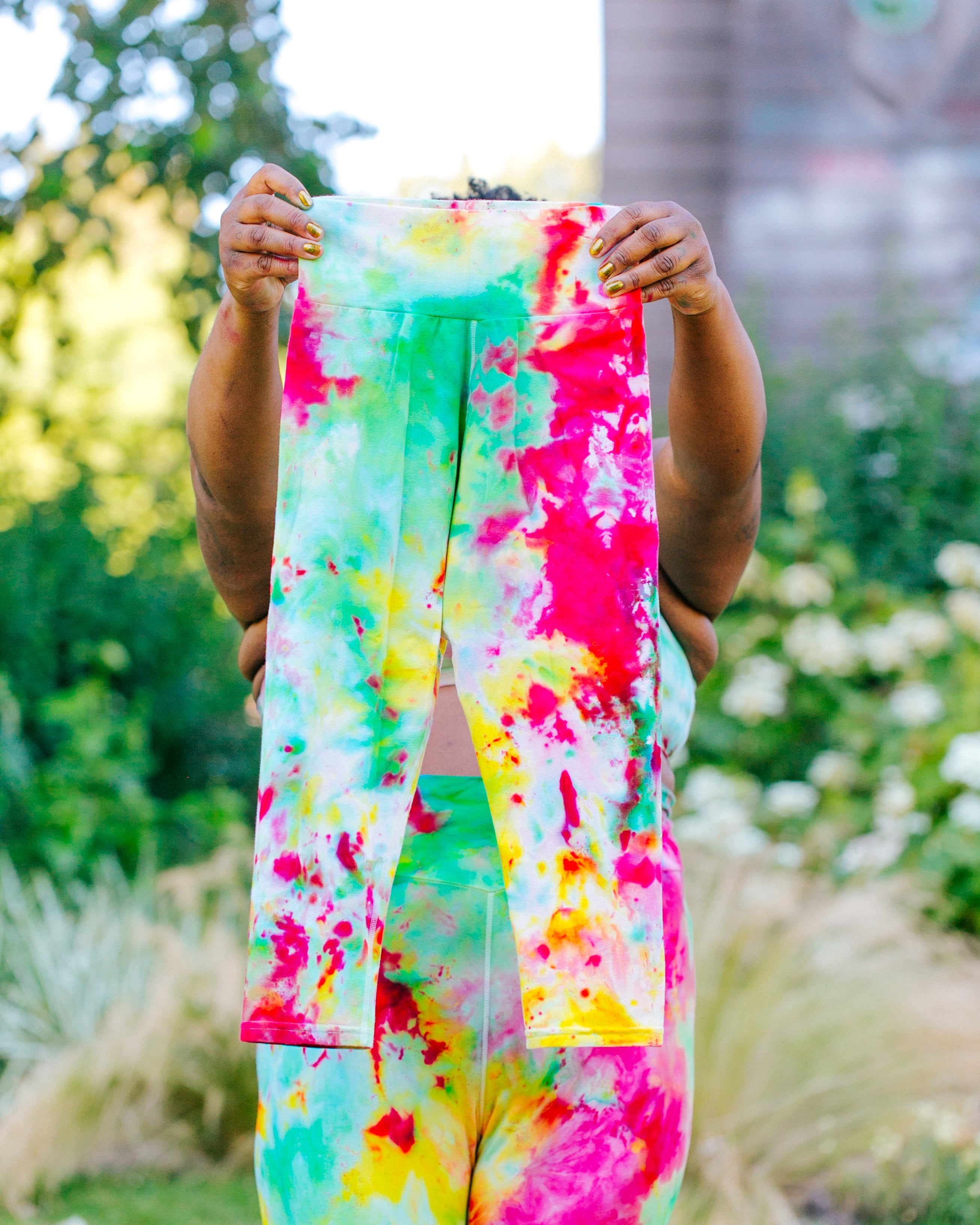 Model wearing Ice Dyed Bike Shorts holding up Ice Dyed 3/4 Length Leggings in a mix of green, pink, and yellow colors.