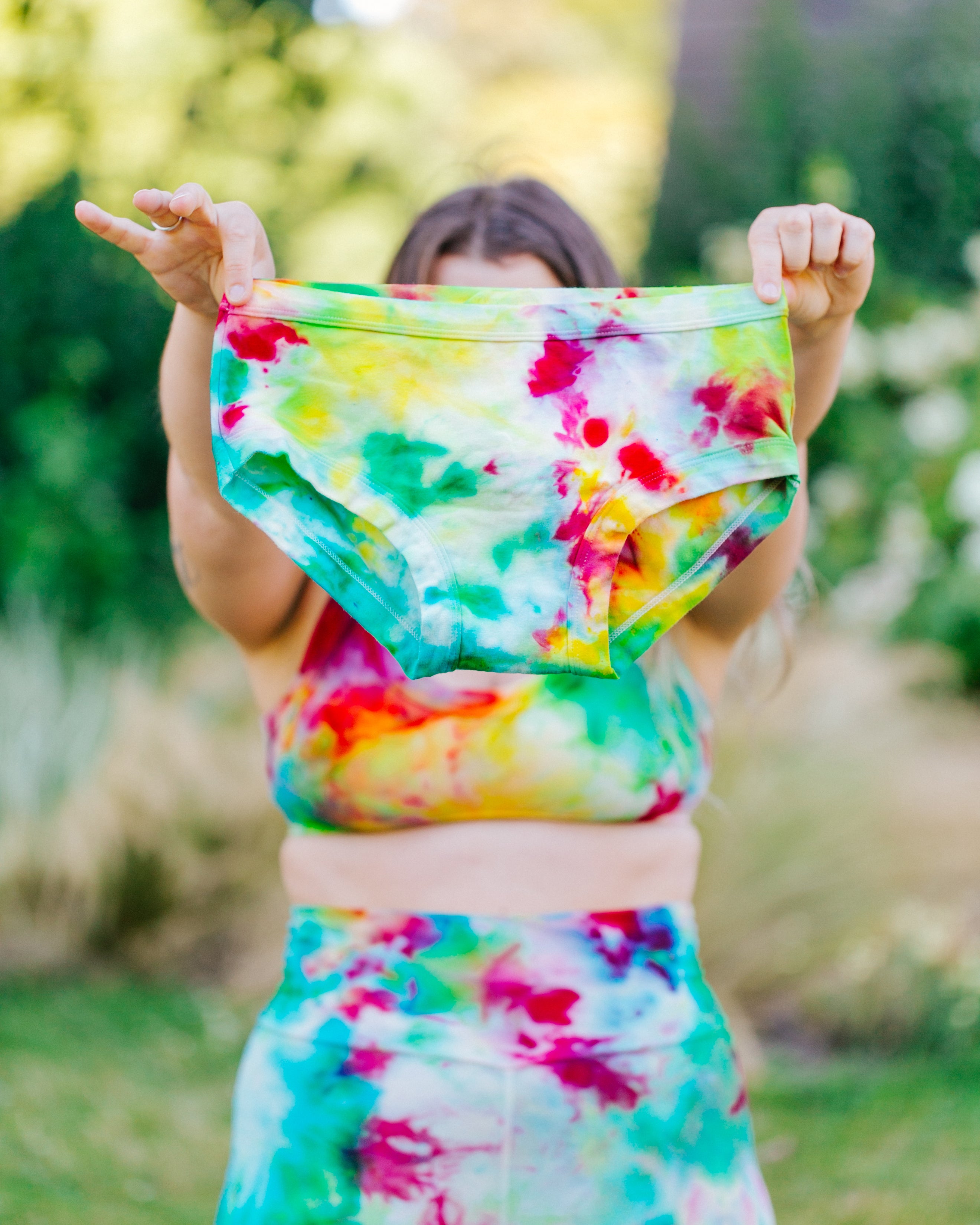 Model wearing ice Dyed Bralette and Bike Shorts holding up Ice Dyed Hipster style underwear in a mix of pink, green, and yellow colors.