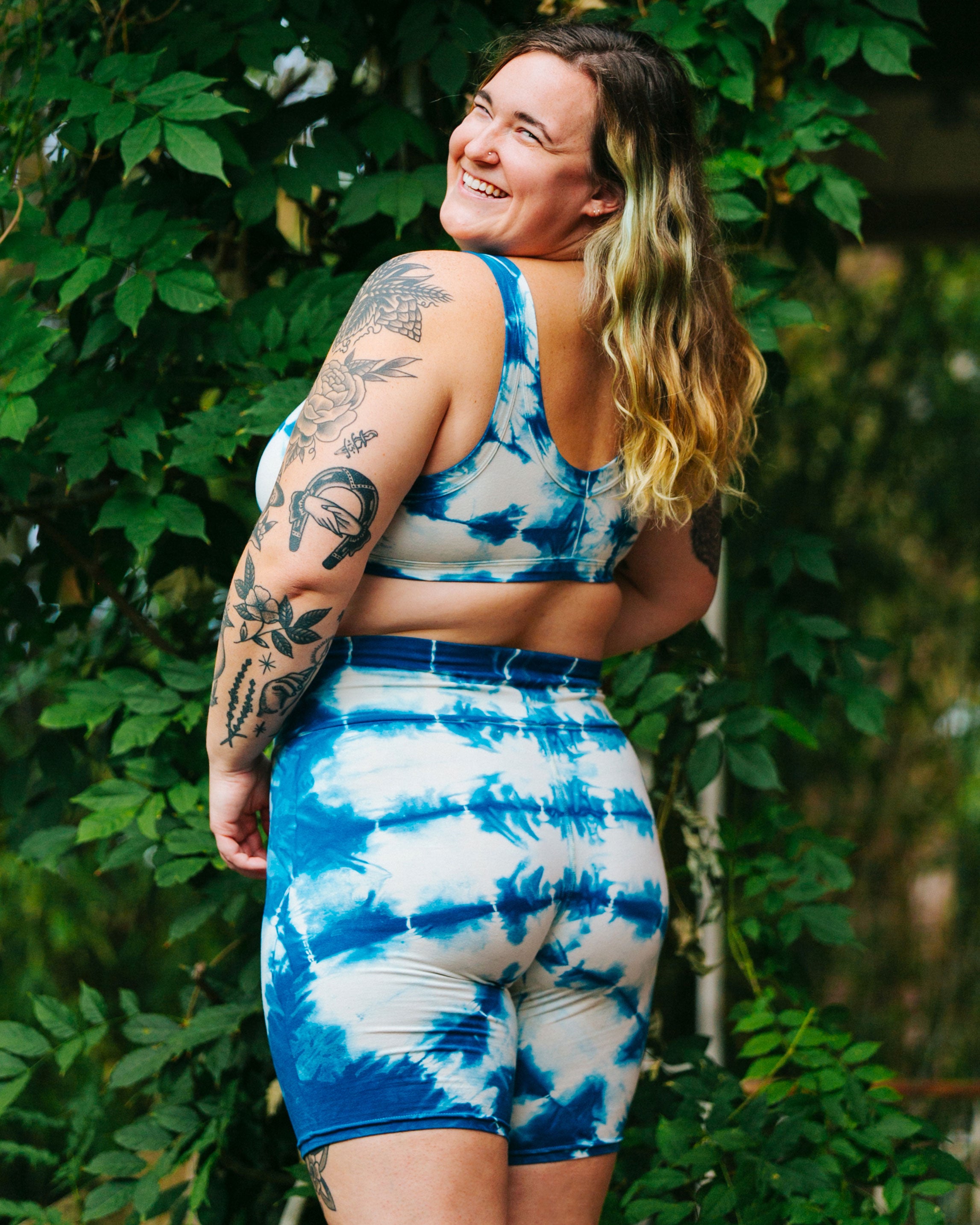 Photo from the back of Thunderpants Organic Cotton Bralette and Bike Shorts in Shibori hand dyed Indigo on a smiling model standing outside.