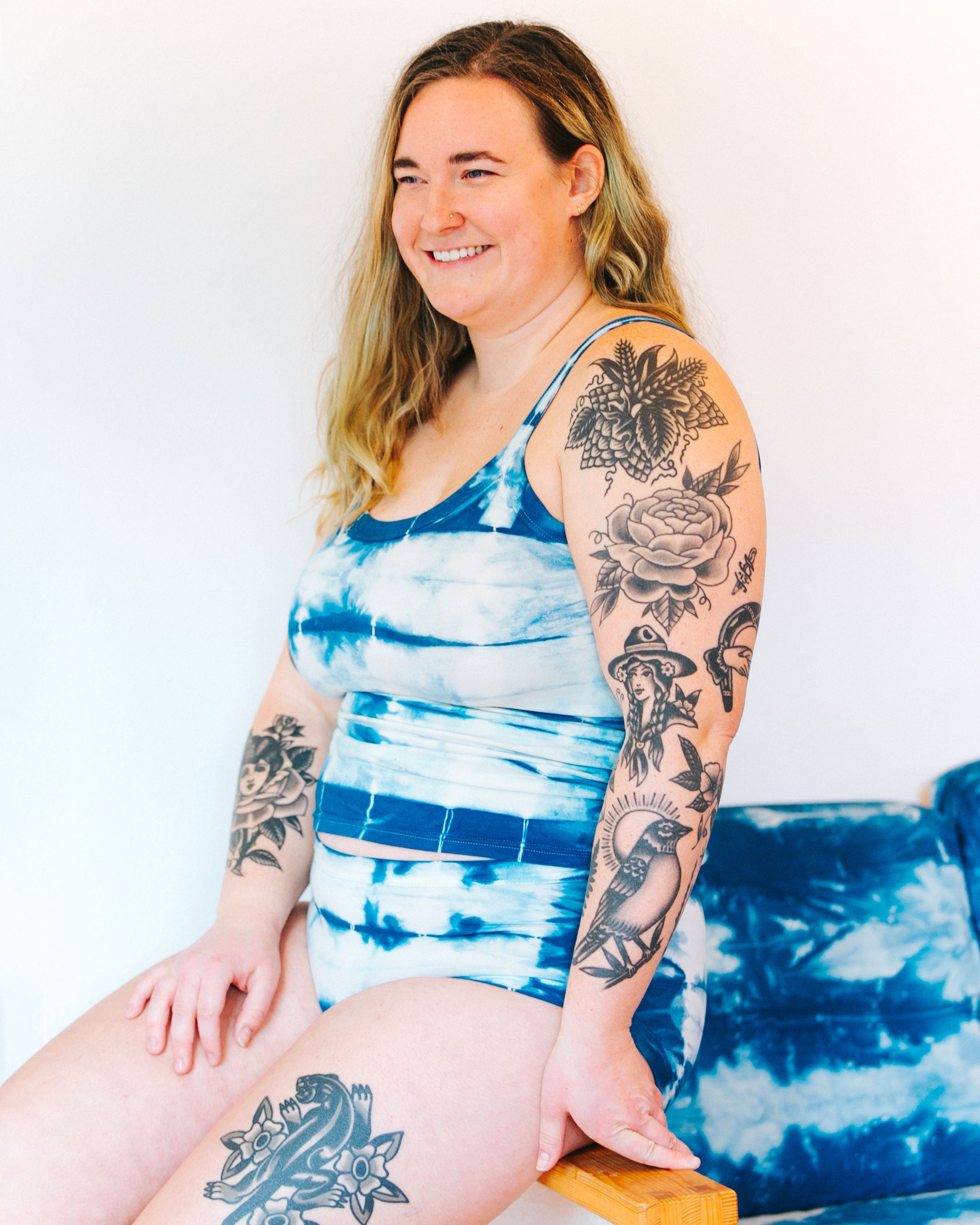 Photo from the front of Thunderpants organic cotton Hipster style underwear and Camisole in shibori hand dyed Indigo on a smiling model sitting on a shibori indigo couch.