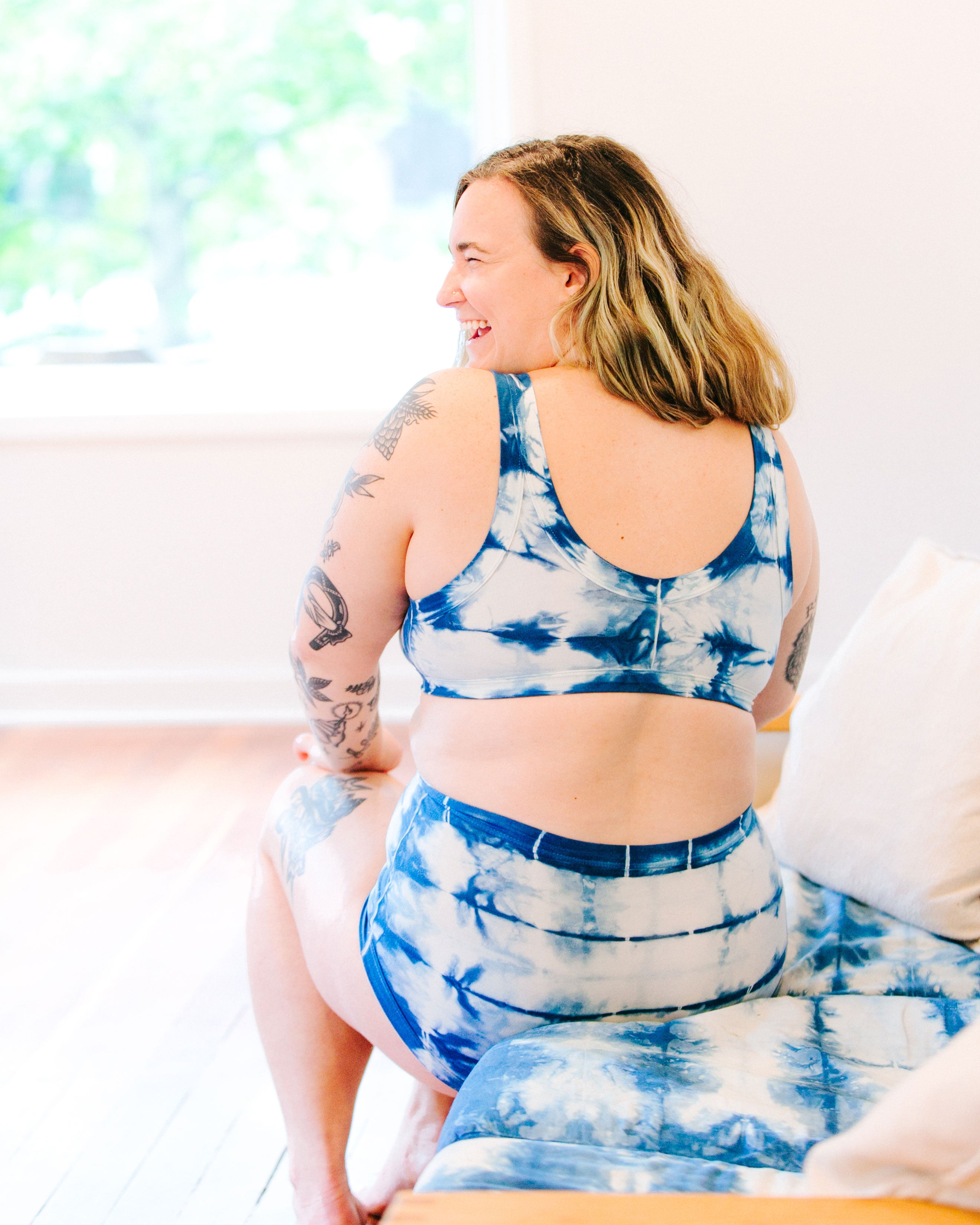 Photo from the back of Thunderpants organic cotton Bralette and Original style underwear in Shibori Hand Dyed Indigo on a model sitting on a shibori indigo couch.