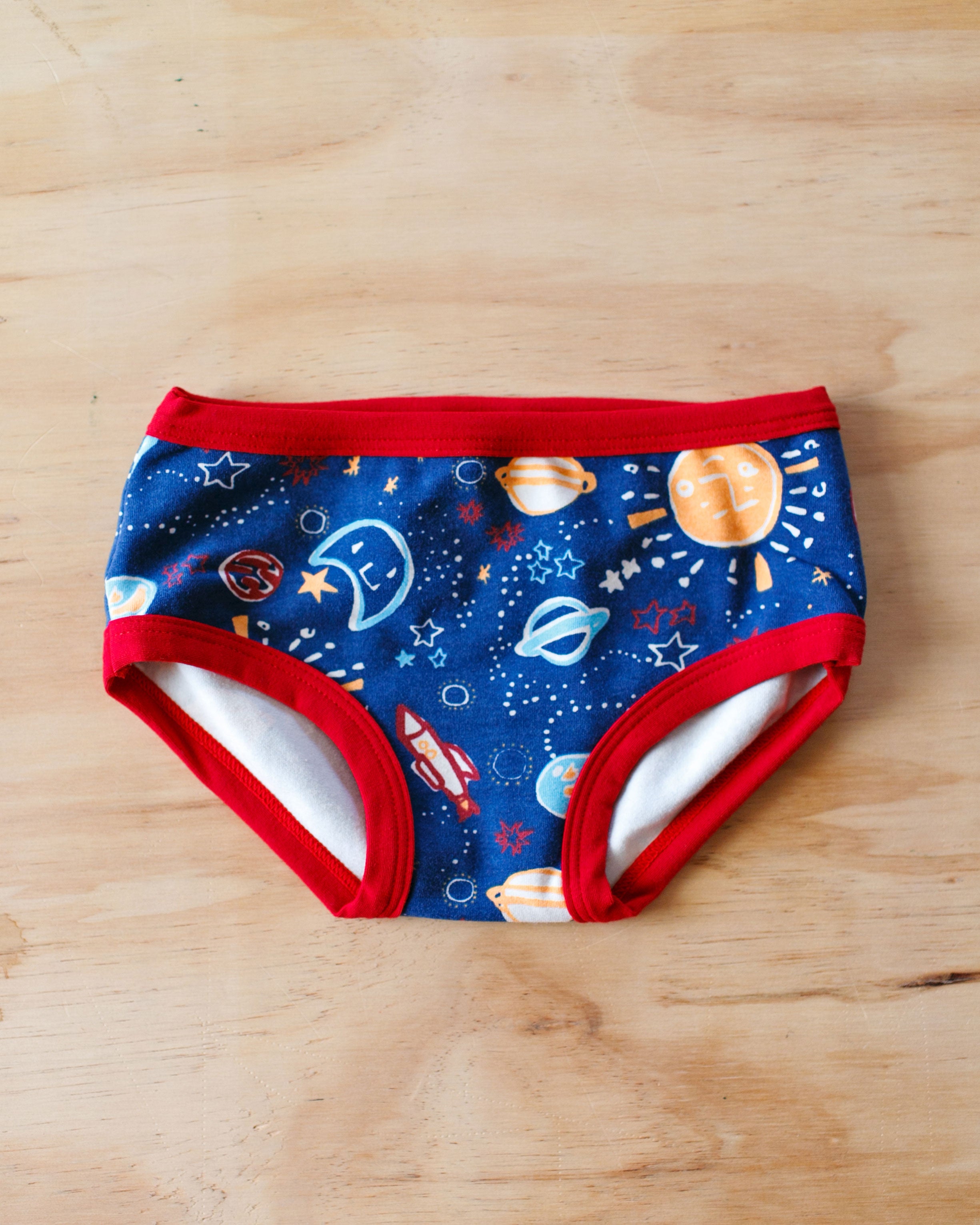 Flat lay of Thunderpants organic cotton Kids underwear in our Dark Sky print: Colorful universe illustrations with red binding.