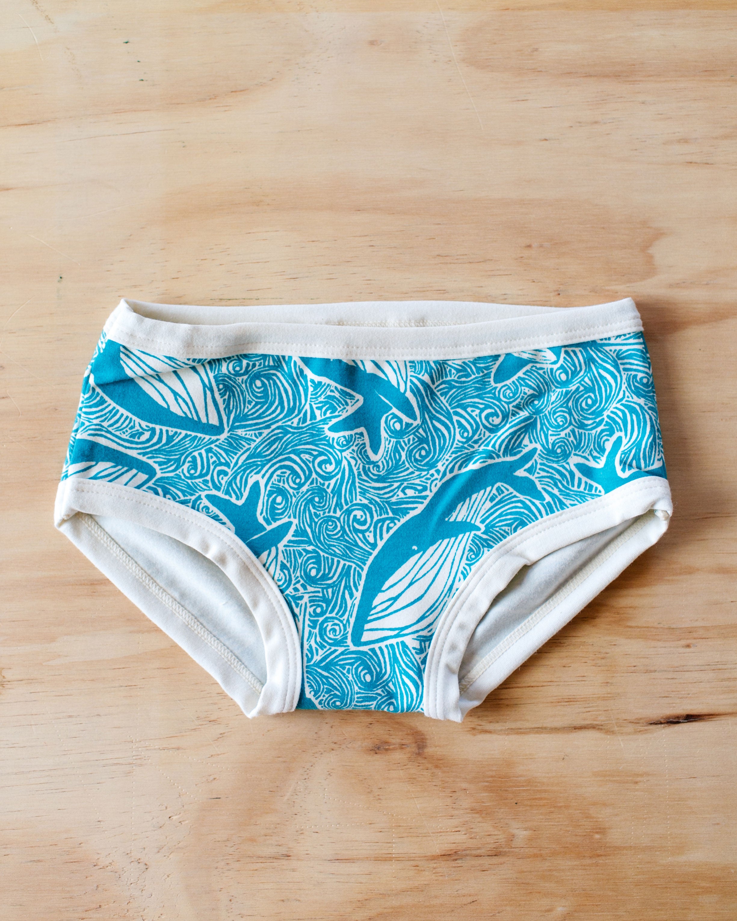 Flat lay of Thunderpants organic cotton Kids underwear in our Marine Whale print: teal whales and ocean with Vanilla binding.