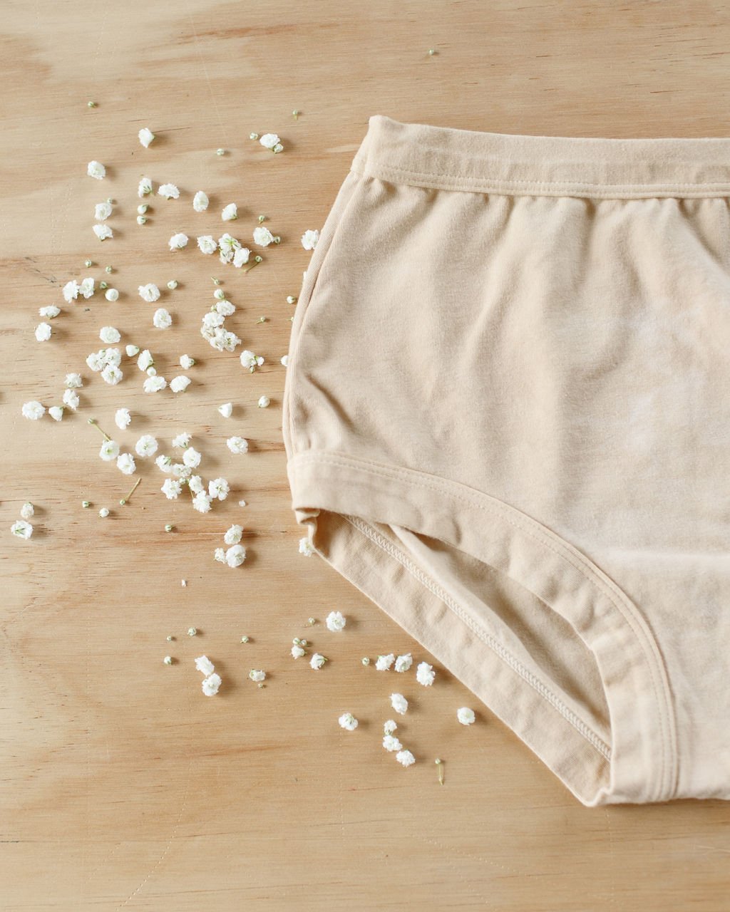 Flat lay of Thunderpants Organic Cotton Original underwear in hand dyed Latte color with white flowers  around.