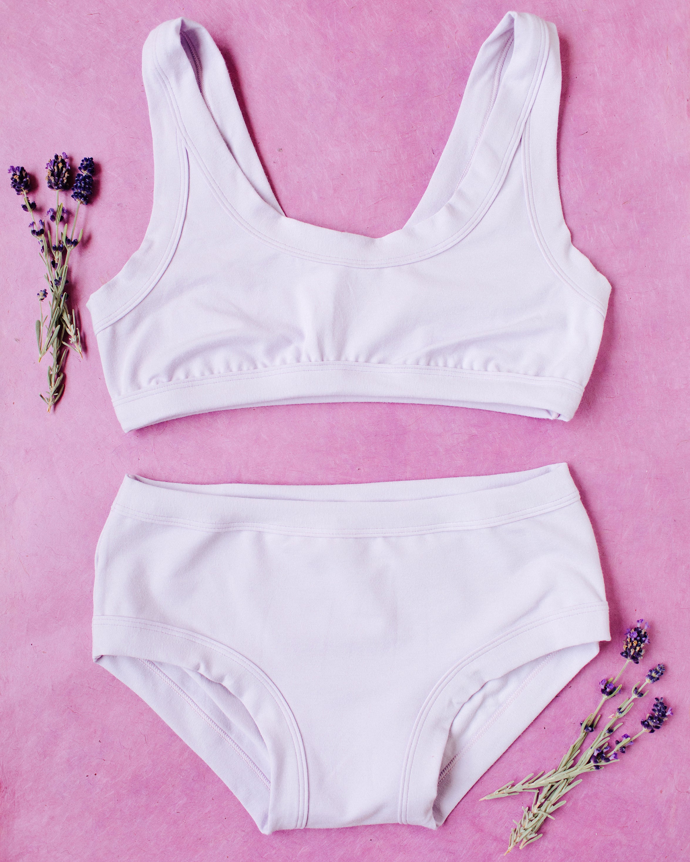 Flat lay of Light Lavender Hipster style underwear and Bralette on a purple surface with lavender sprigs.