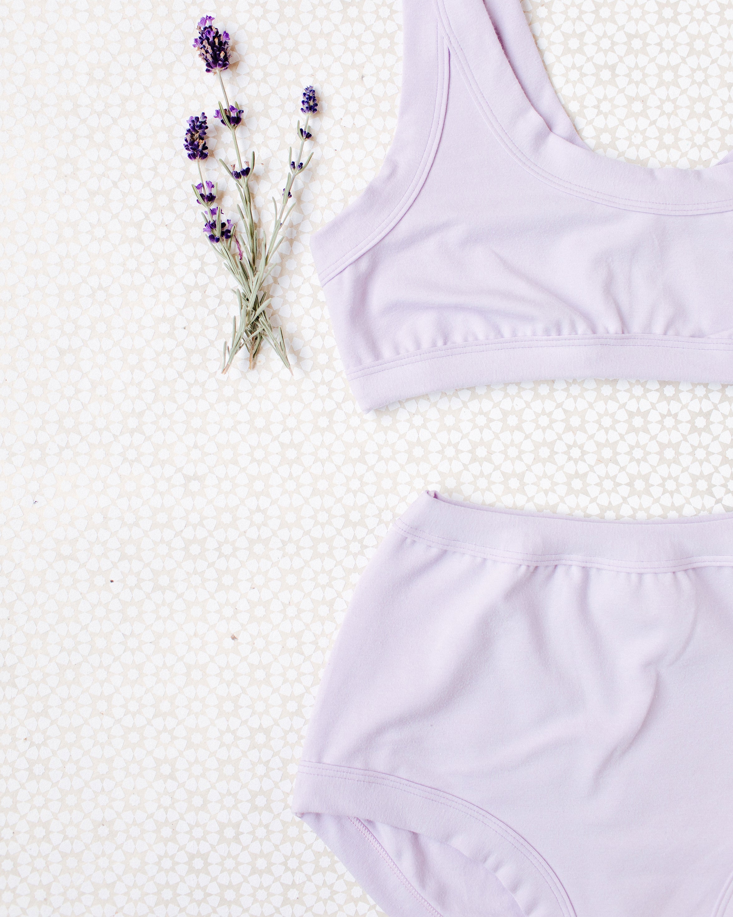 Close up flat lay of Light Lavender Original style underwear and Bralette on a white patterned surface with lavender sprigs.