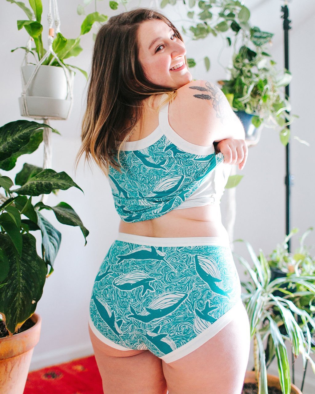 Model smiling over her shoulder wearing Thunderpants organic cotton Original style underwear, showing a wedgie-free bum, and a Camisole in our Marine Whale print: turquoise whales and ocean all over print.