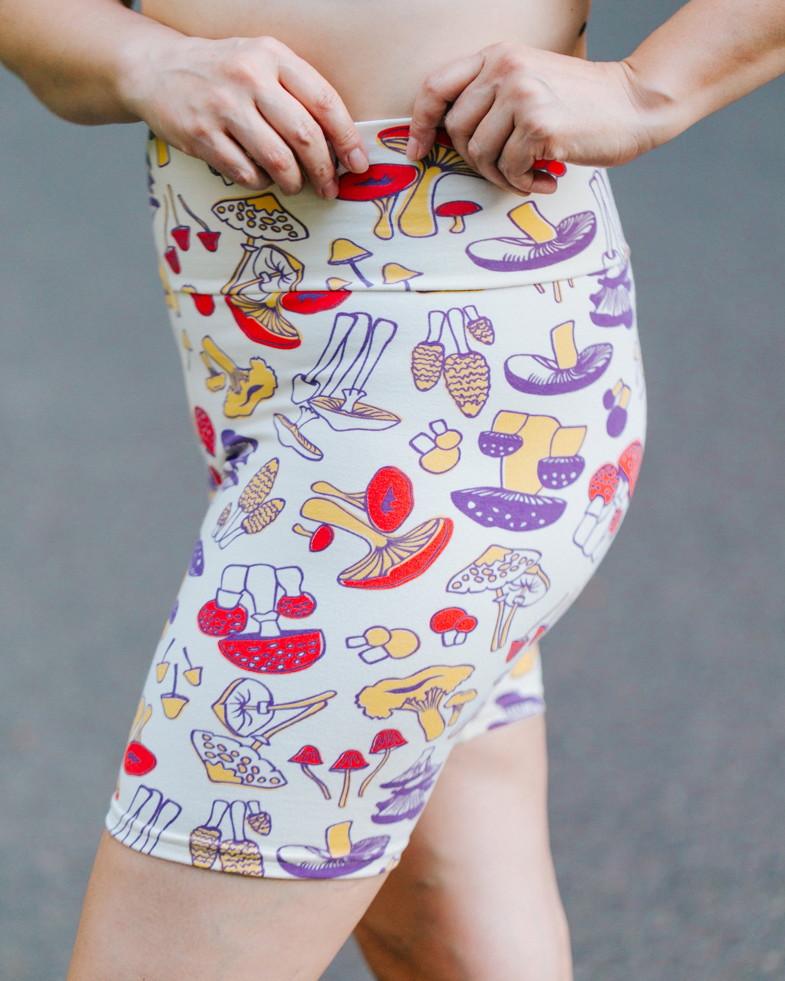 Close up of model wearing Bike Shorts in Mushroom Magic print: different kinds of mushrooms in yellow, red, and purple colors.