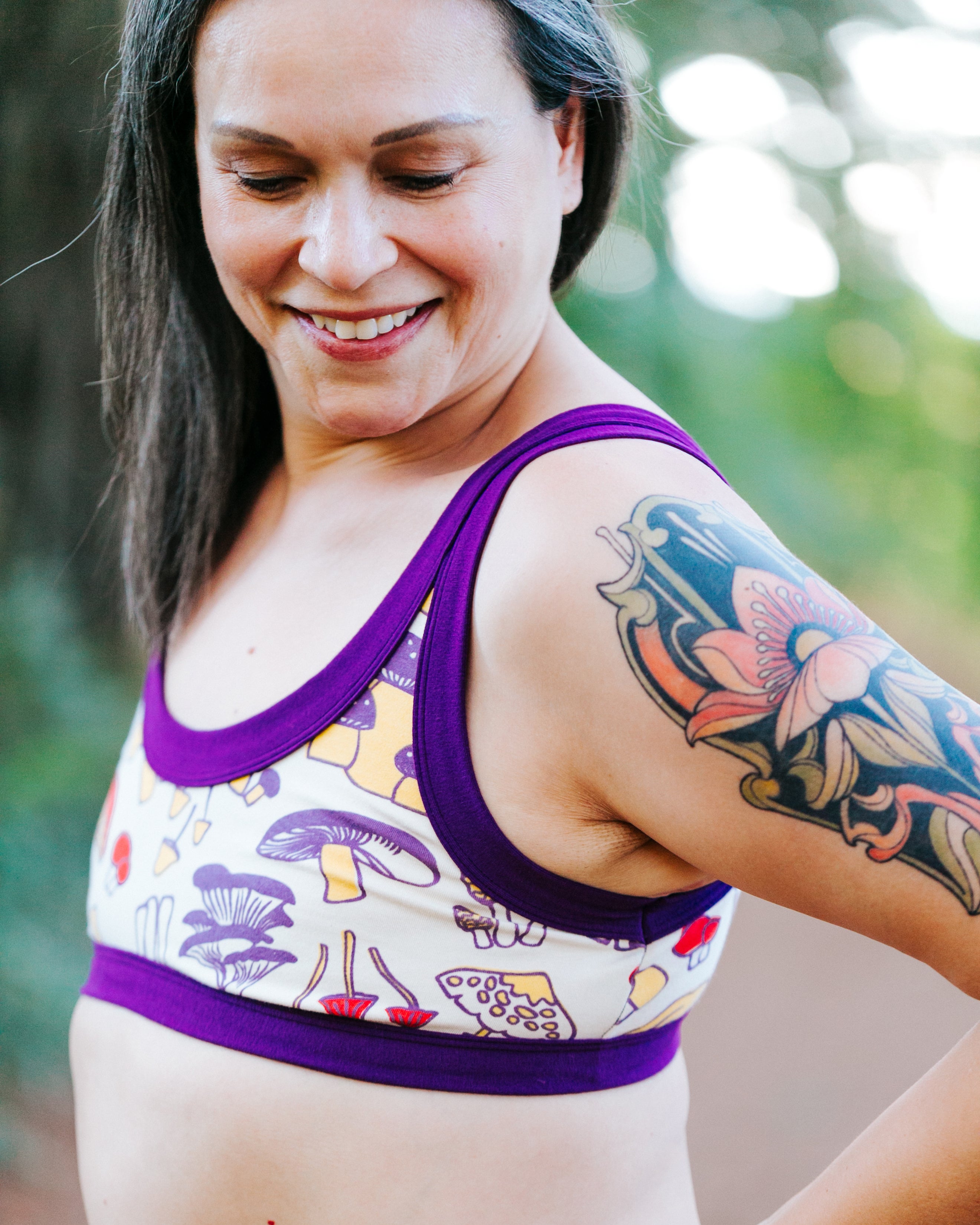Close up of model wearing Bralette in Mushroom Magic print: different kinds of mushrooms in red, yellow, and purple colors with dark purple binding.