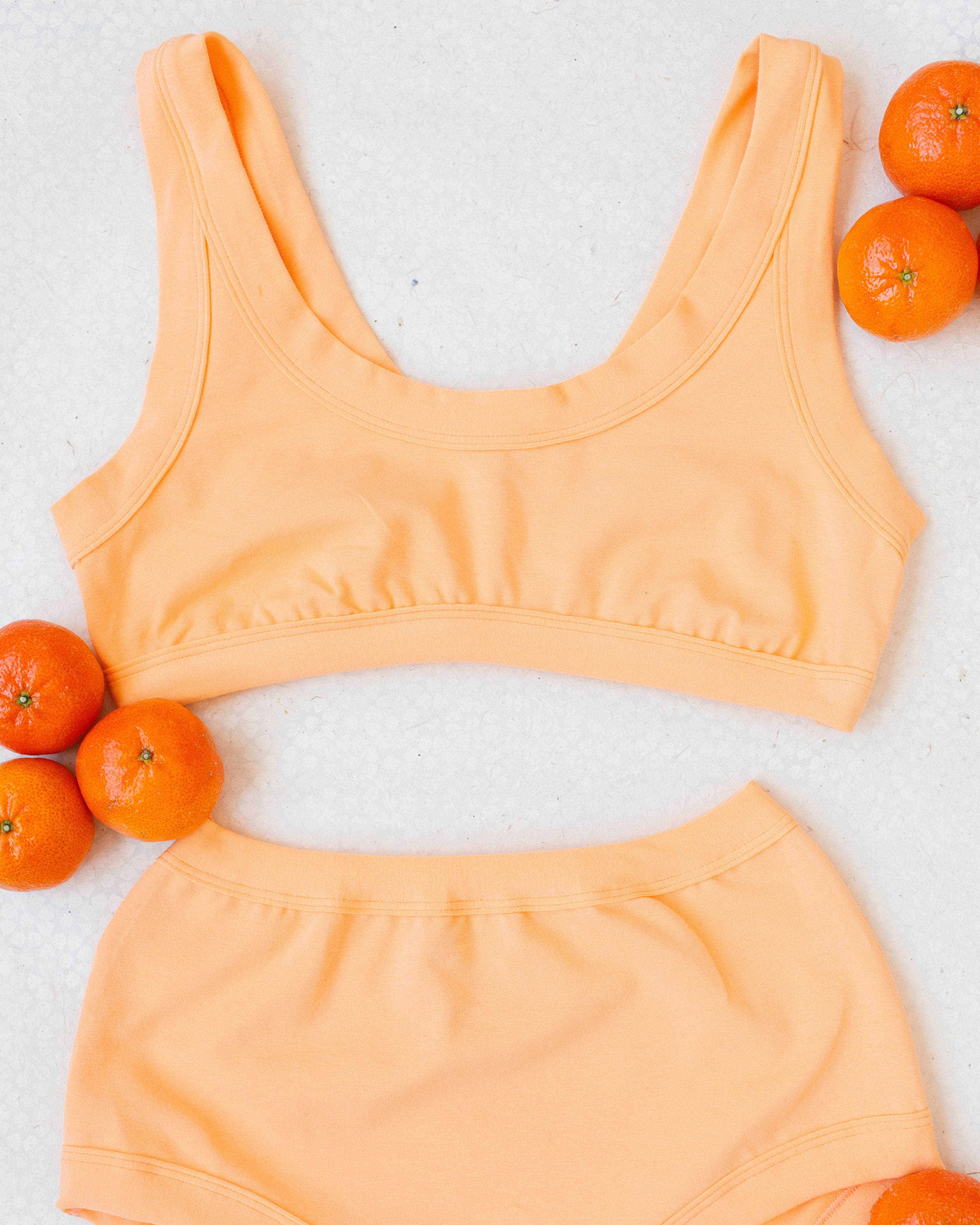 Flat lay of Orange Sherbet Bralette on a white surface with oranges around it.