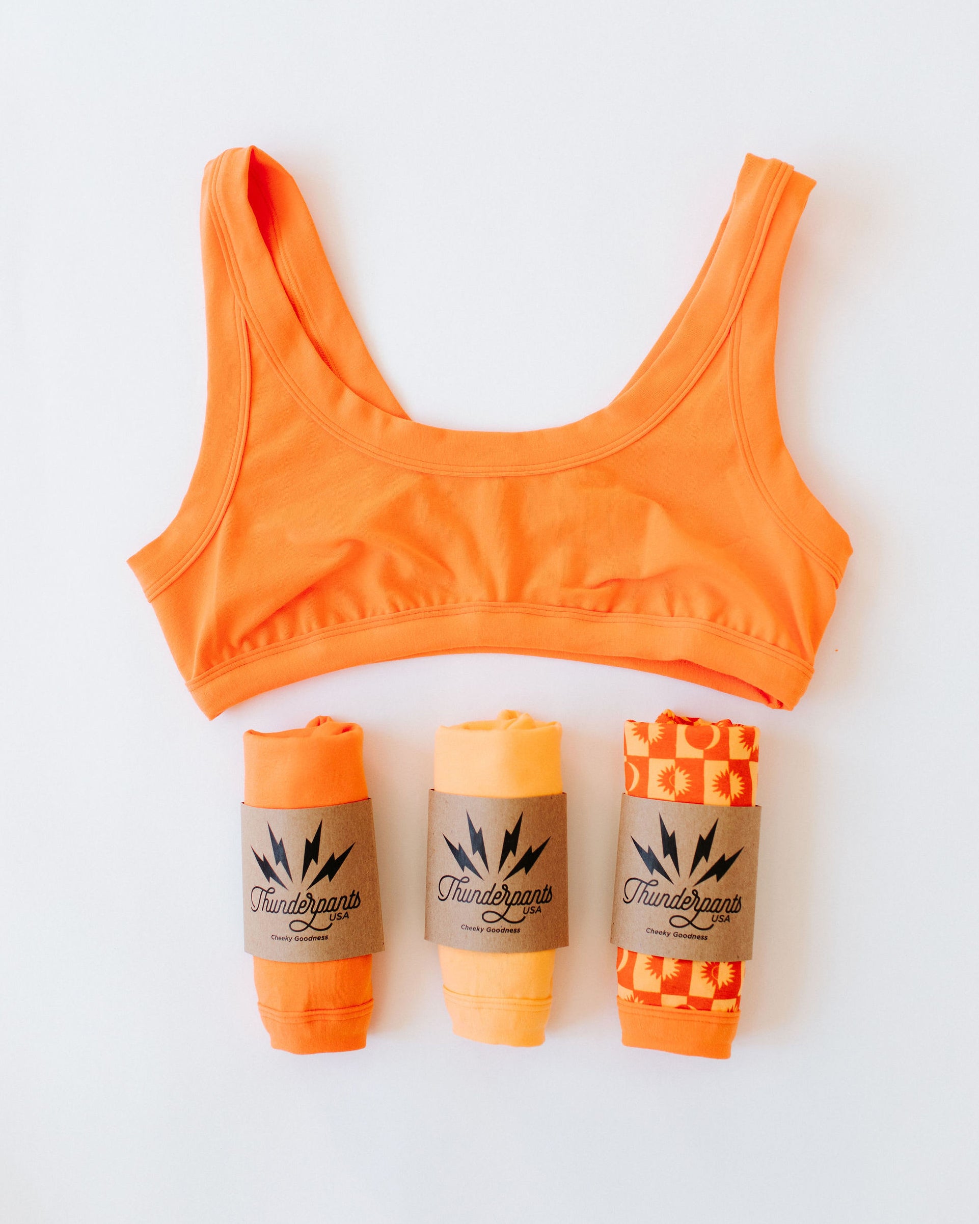 Flat lay of Thunderpants Bralette and three packaged underwear in Oregon Sunstone orange color.