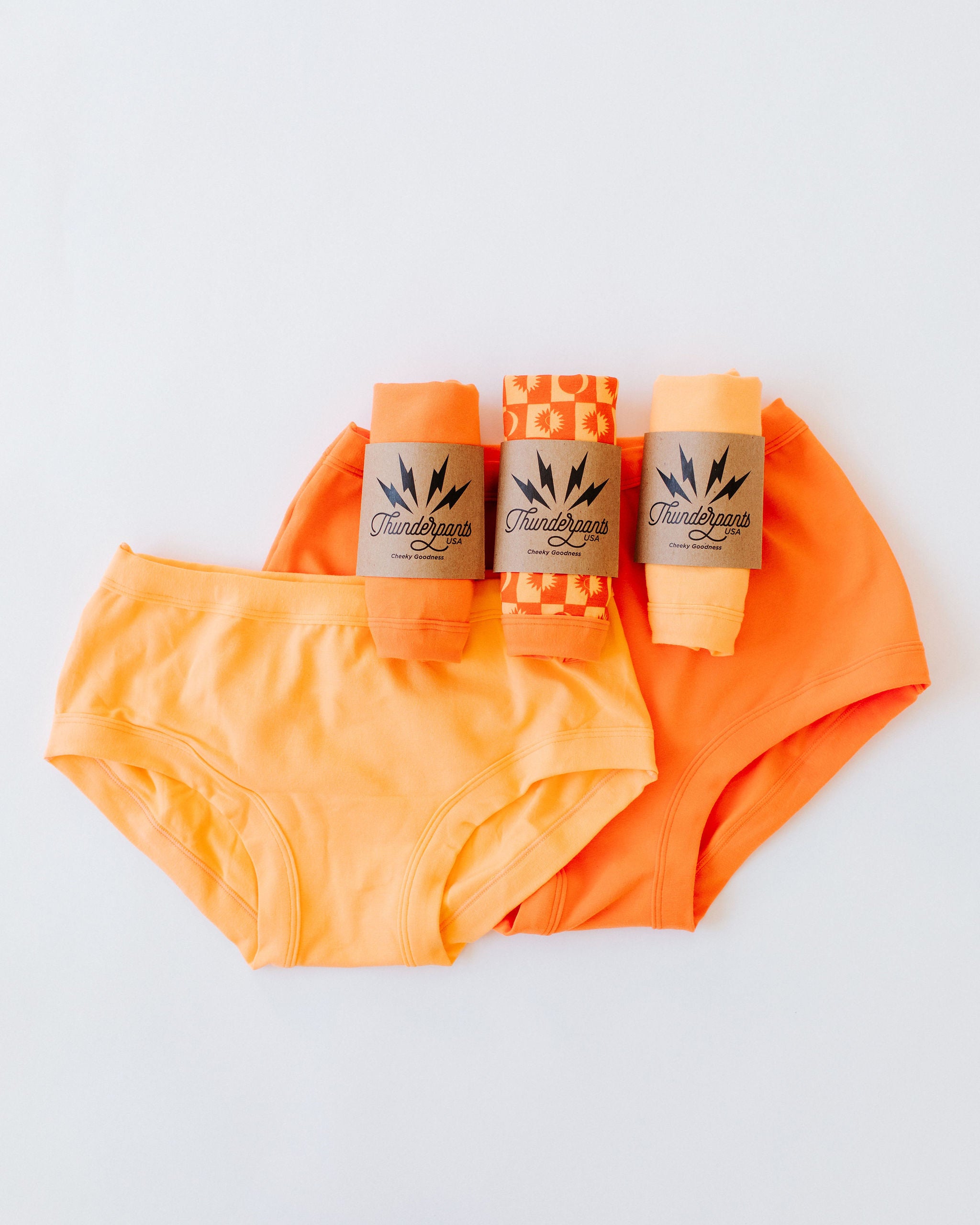Flat lay of Thunderpants Hipster and Original style underwear with three packaged pairs in various orange colors.