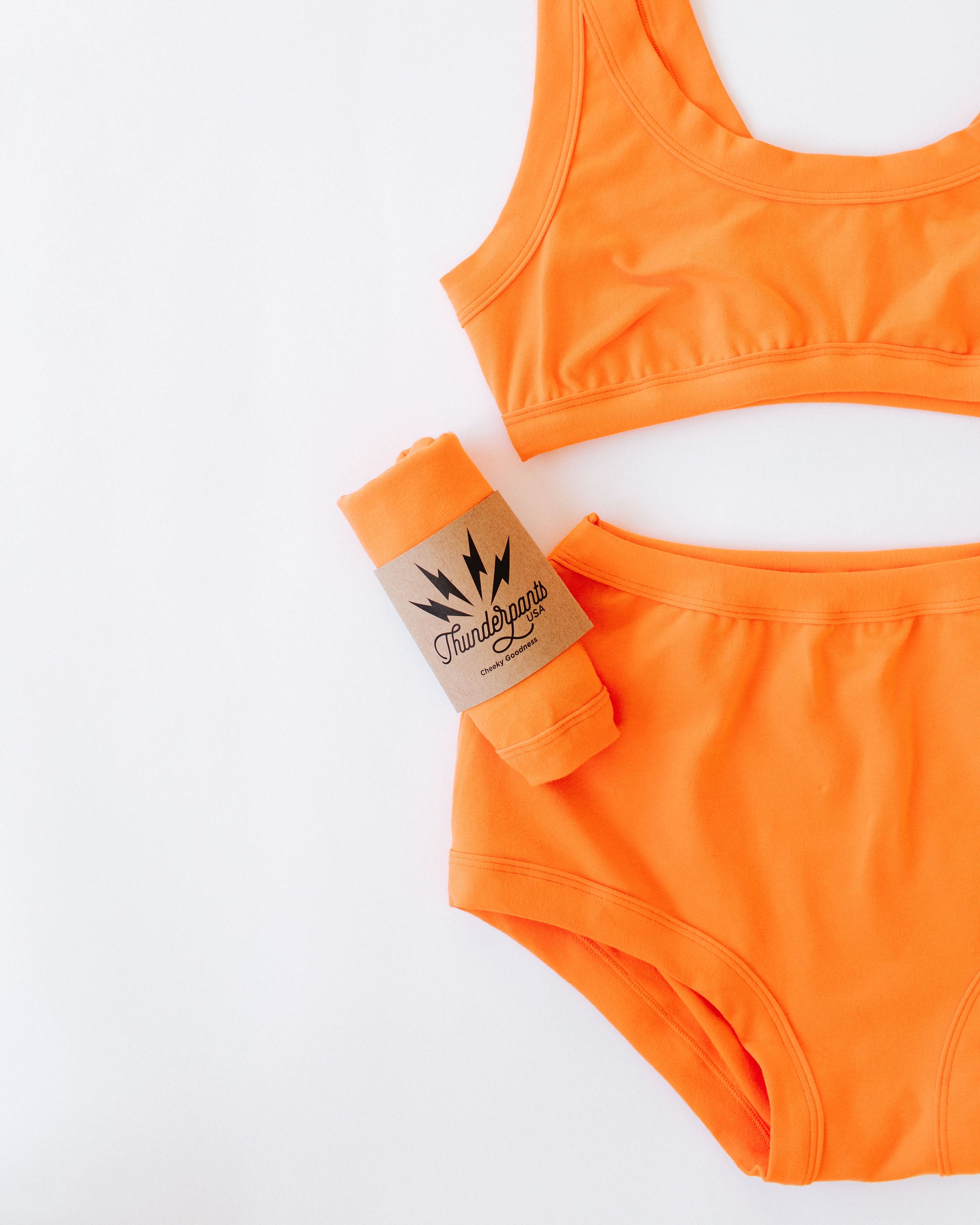 Closeup flat lay of Thunderpants Original style underwear and Bralette in Oregon Sunstone orange color.