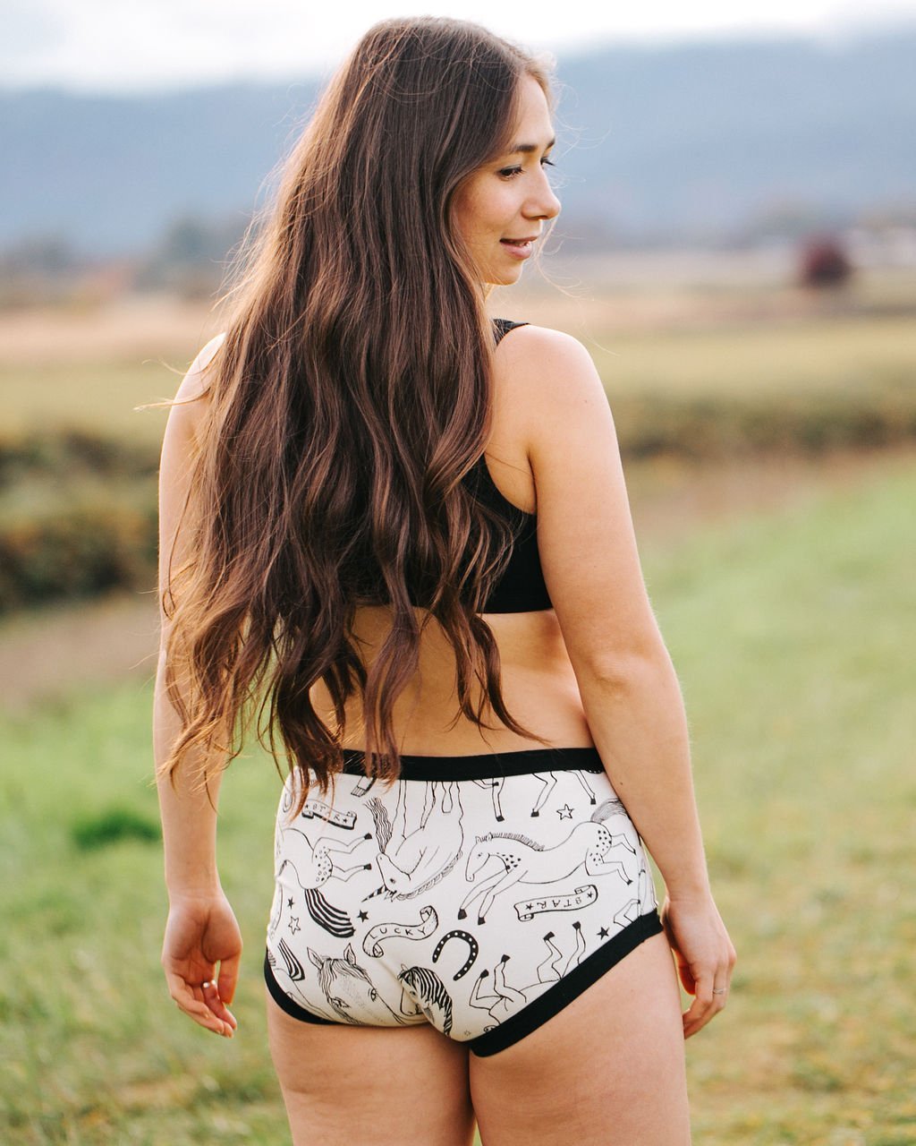 Back of woman with long hair wearing Thunderpants organic cotton Original style underwear, showing a wedgie-free bum, in a black and white horses print.