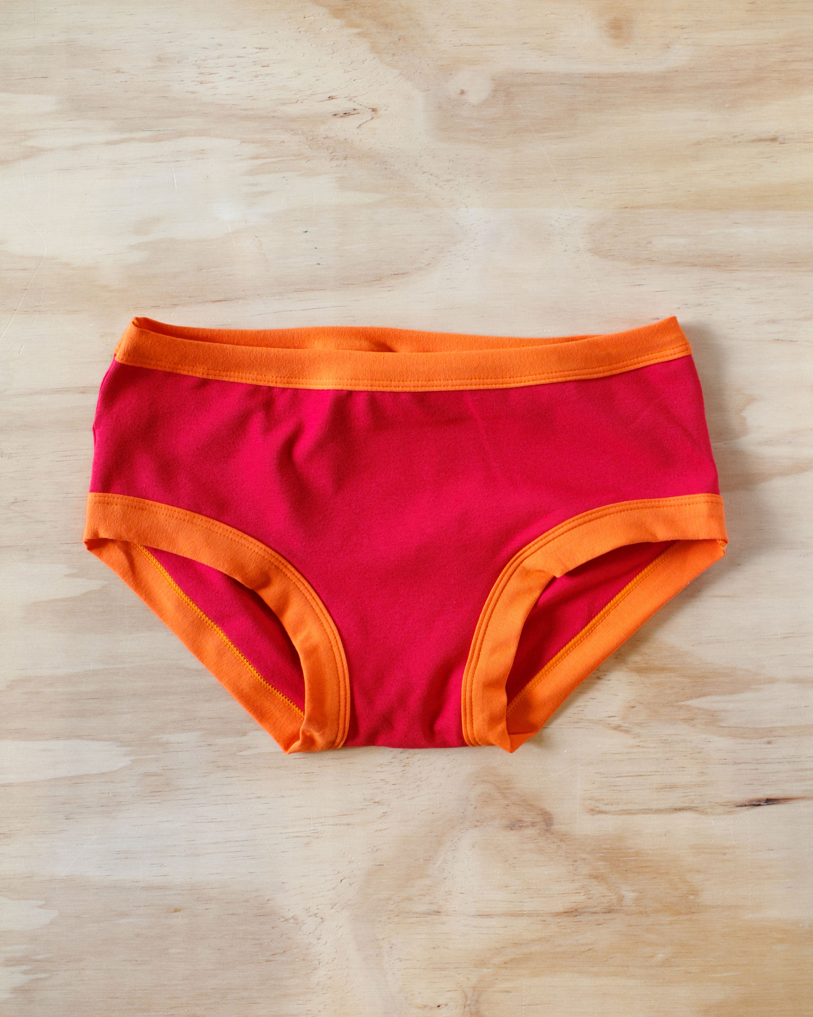 Flat lay on wood surface of Hipster Pants on Fire: red with orange binding.