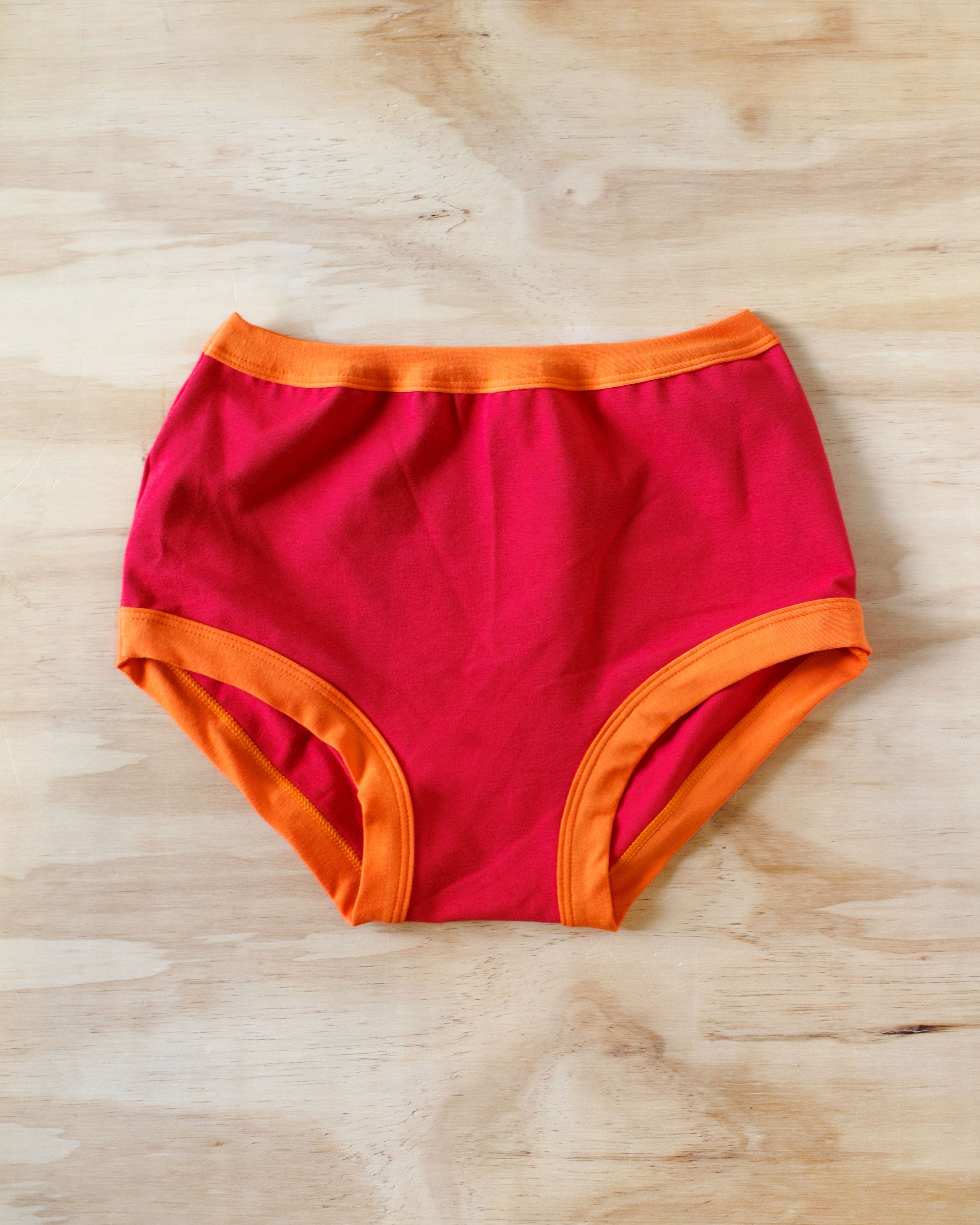 Flat lay on wood surface of Original style Pants on Fire: red with orange binding.