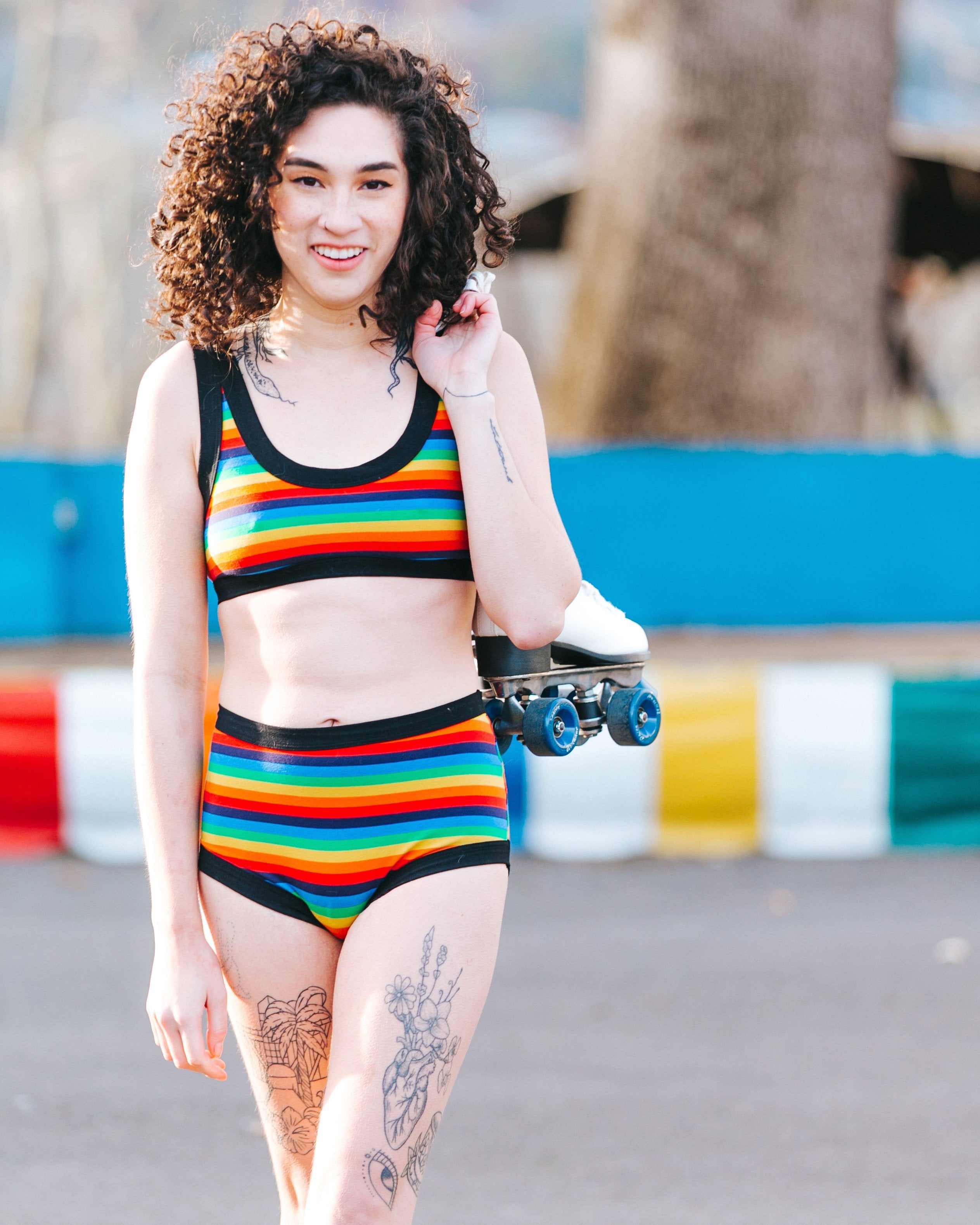 Happy model with roller skates over her shoulder wearing Thunderpants organic cotton Original style underwear and Bralette in Rainbow Stripes.