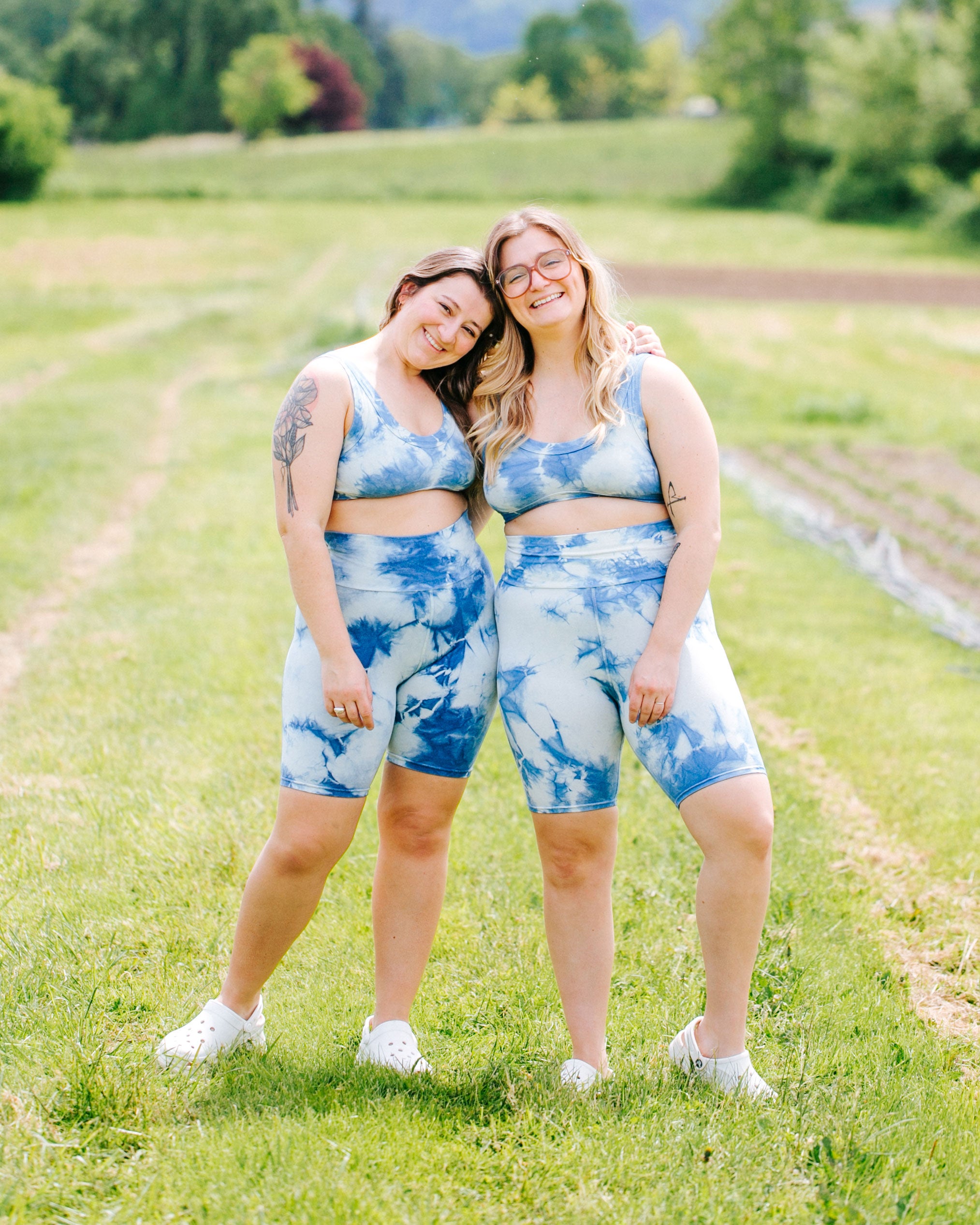Two models smiling together in a field of green wearing indigo dyed Sauvie Skies Bike Shorts and Bralettes.