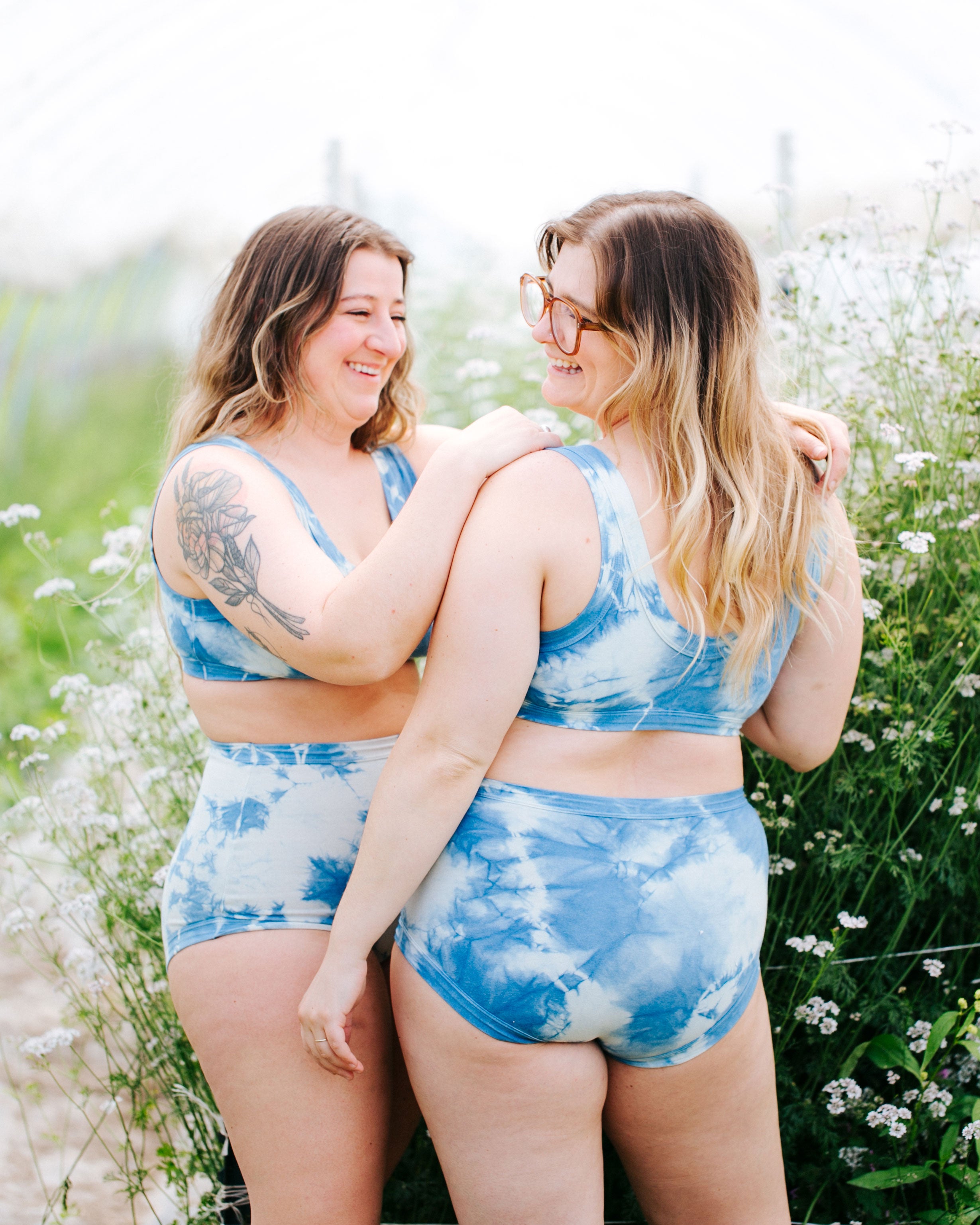 Two models smiling in a greenhouse wearing sets of indigo dyed Sauvie Skies underwear in Orignial style and Bralettes.