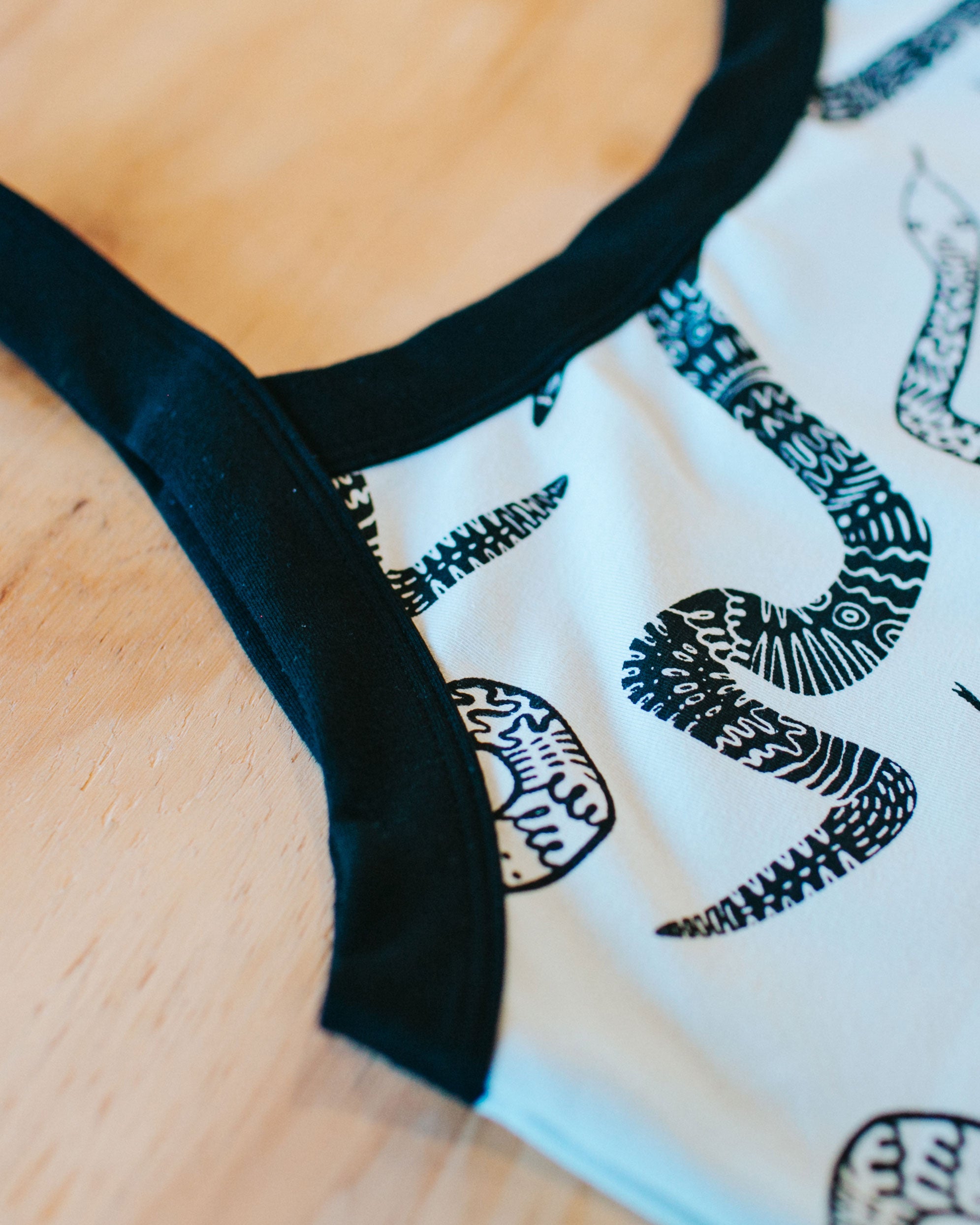 Flat lay close up of our Camisole in the Sketchy Snake pattern: dried sage color with black snakes and black binding.