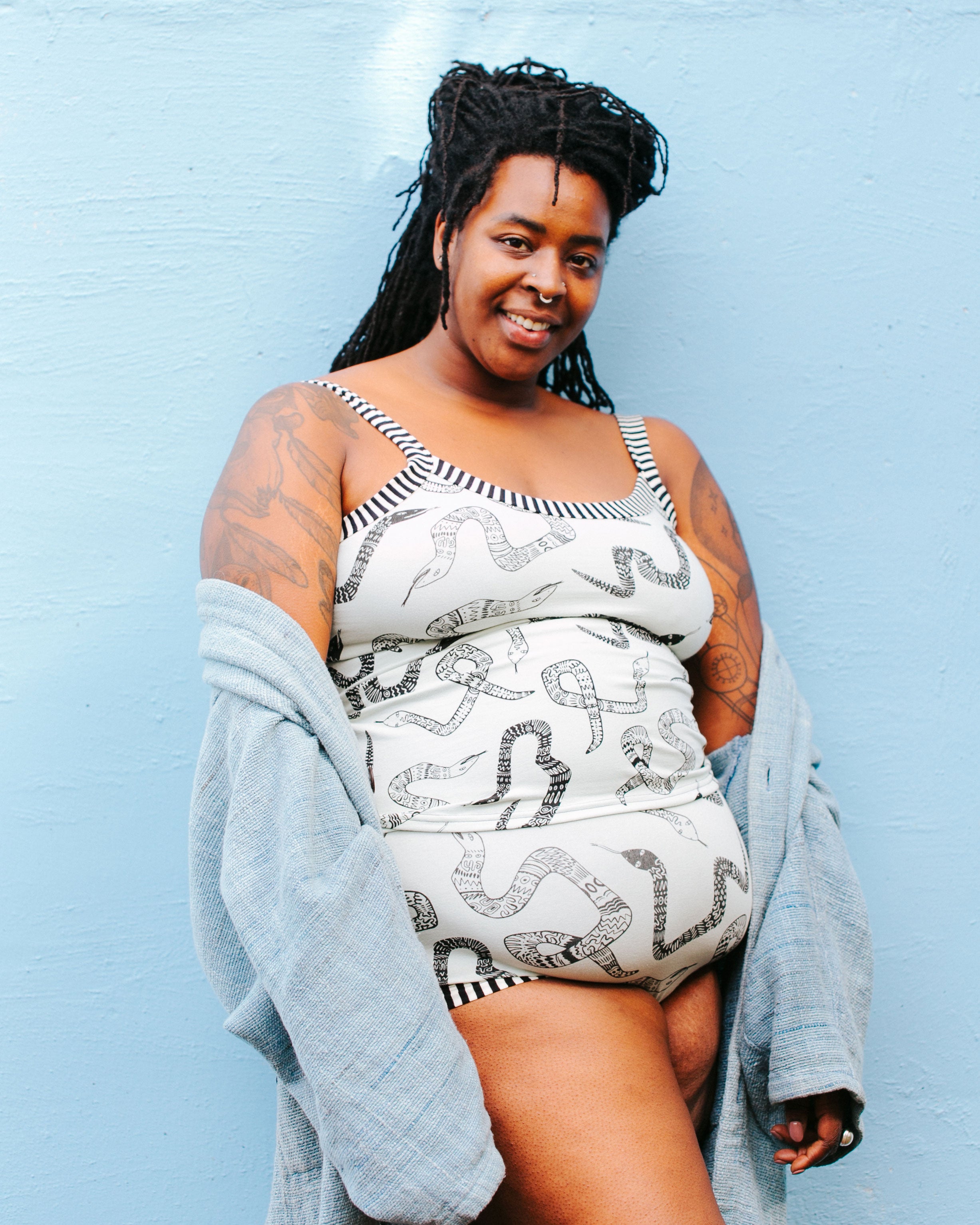 Model smiling at the camera wearing Thunderpants organic cotton Camisole and Original style underwear in our Sketchy Snakes print: sage color with black sketched snakes and black and white stripe binding.