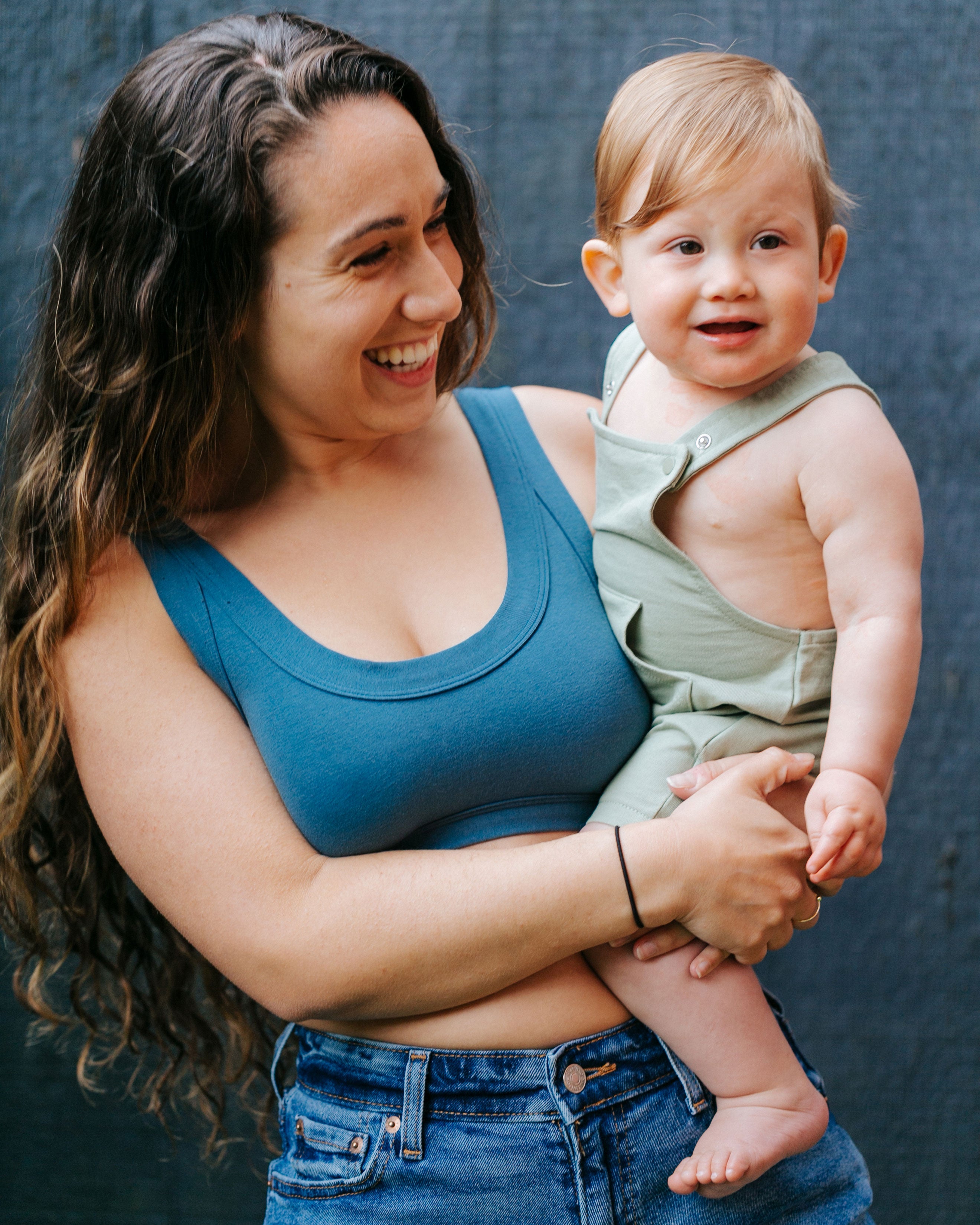Smiling model holding her baby while wearing the Bralette in Stormy Blue and jeans.