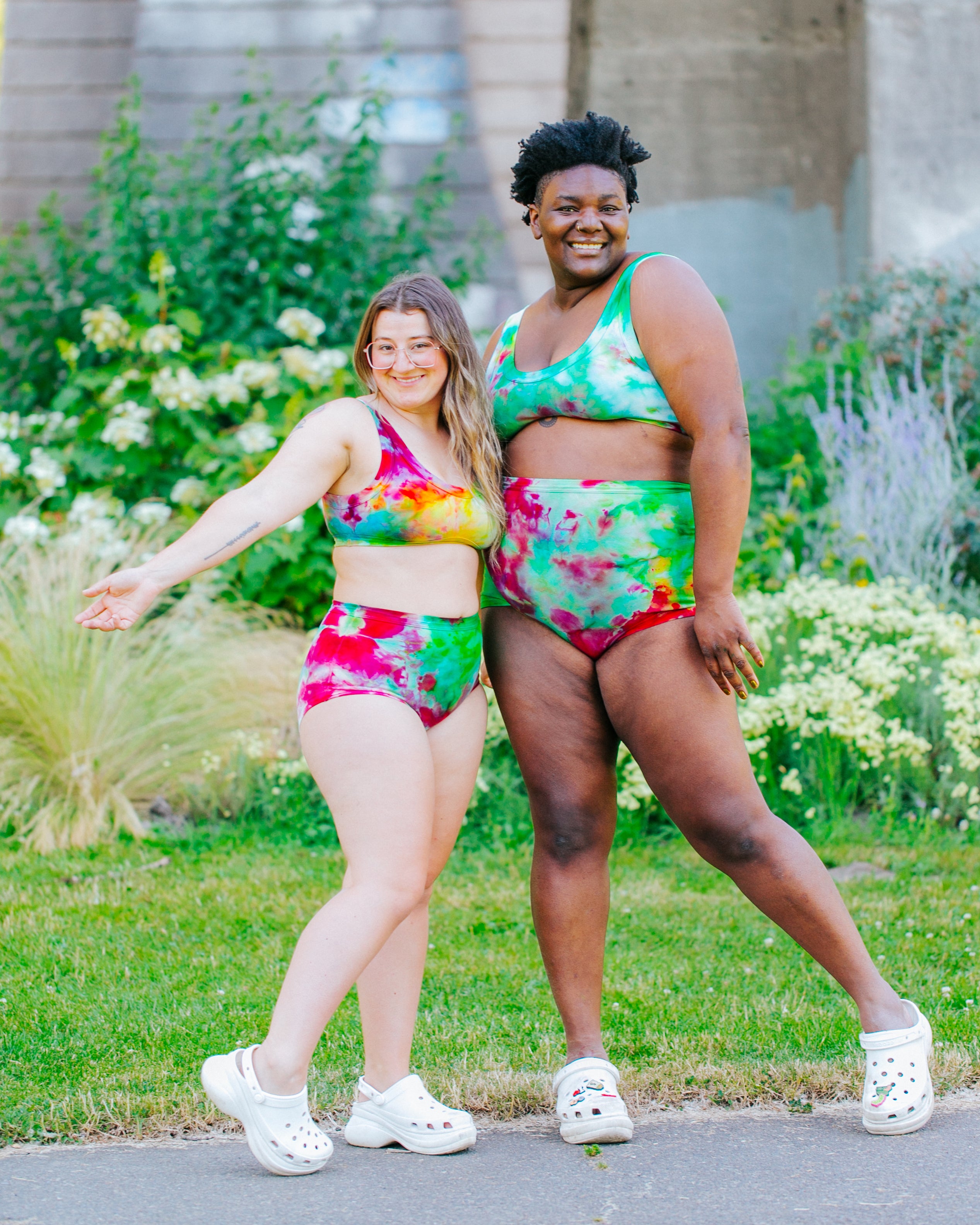 Two models smiling wearing sets of Ice Dye Sky Rise and Original style underwear and Bralettes in a mix of bright pink, yellow, green, and blue colors.