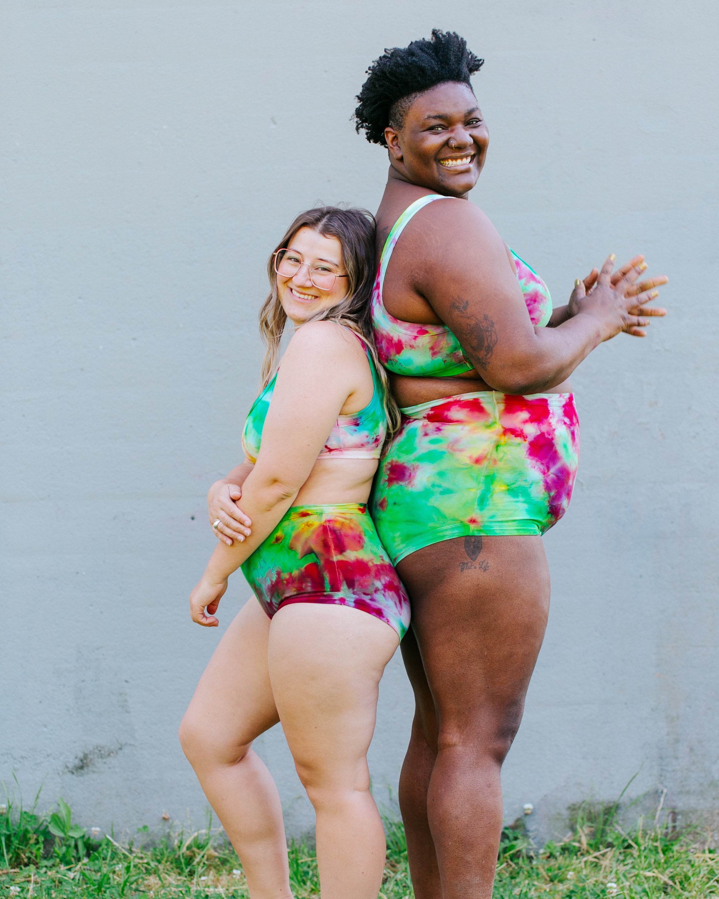 Two models smiling wearing sets of Ice Dyed Original and Sky Rise style underwear and Bralettes in a mix of pink, green, and yellow colors.