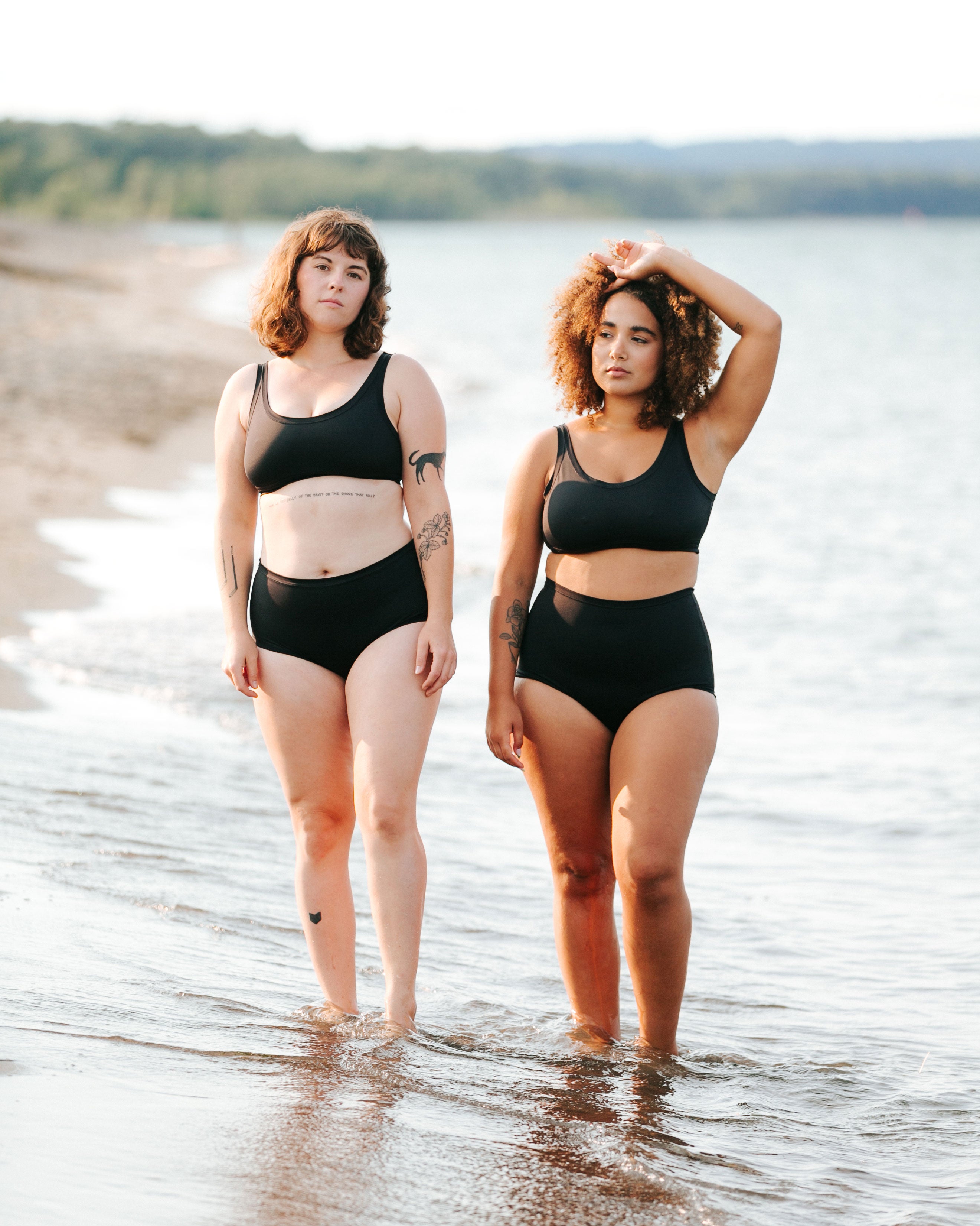 Two models walking on the beach wearing Sky Rise style and Original Style Swimwear Bottoms and Swimwear Tops in Plain Black.