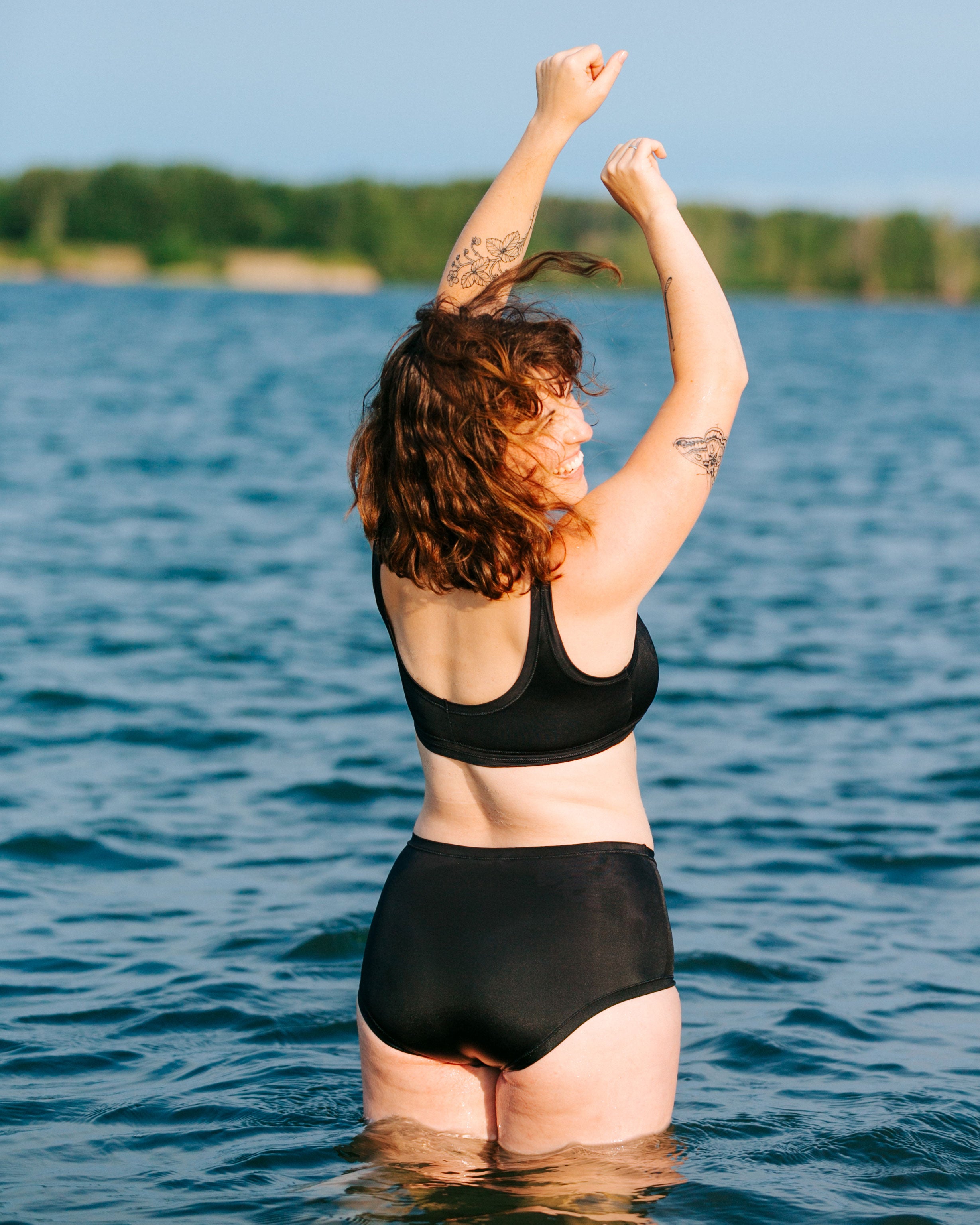 Model standing with back to us in the water wearing Thunderpants recycled nylon Original style Swimwear bottoms and Swimwear Top in Plain Black.