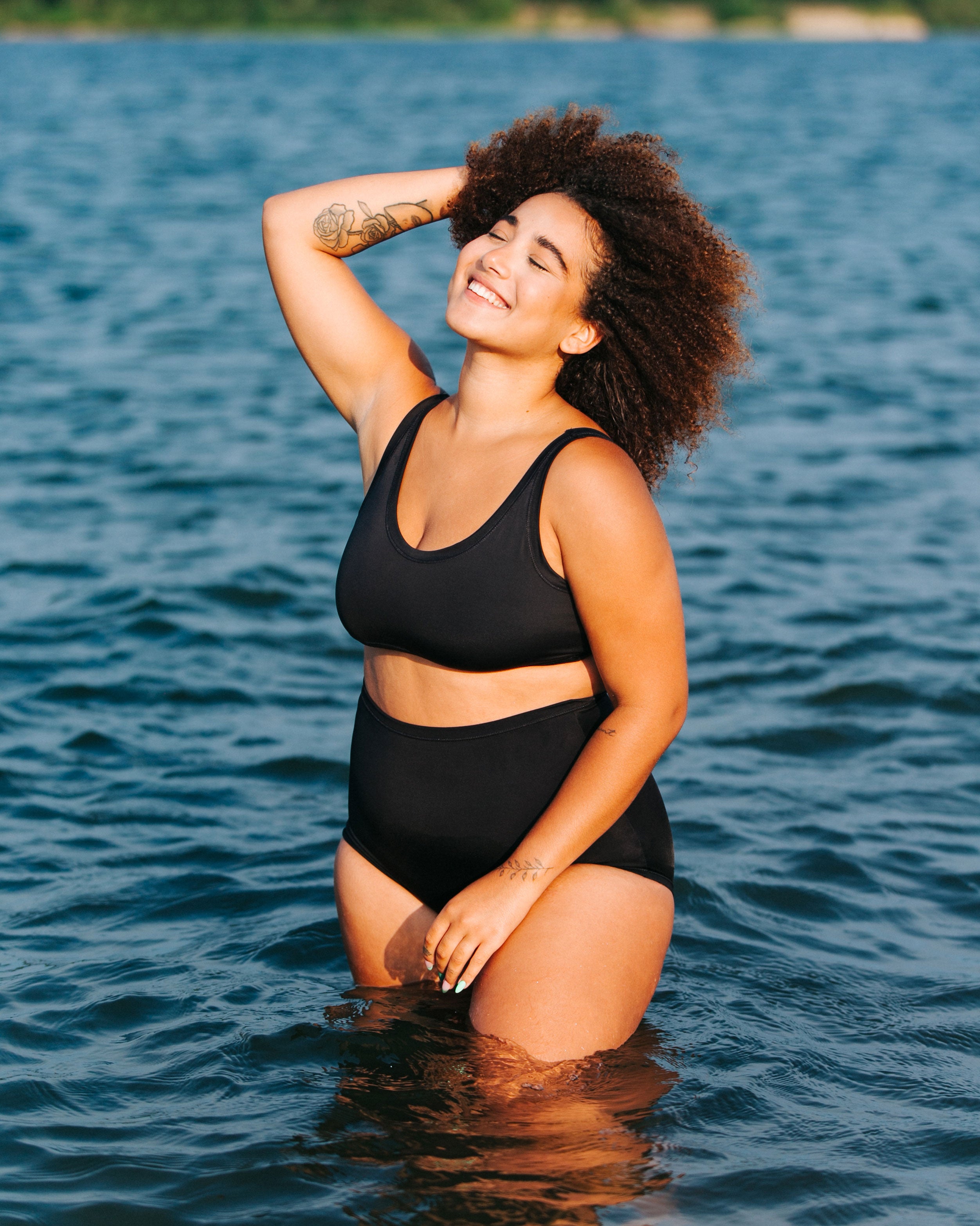 Model in the water smiling and wearing Thunderpants recycled nylon Sky Rise style Swimwear Bottoms and Swimwear Top in Plain Black.