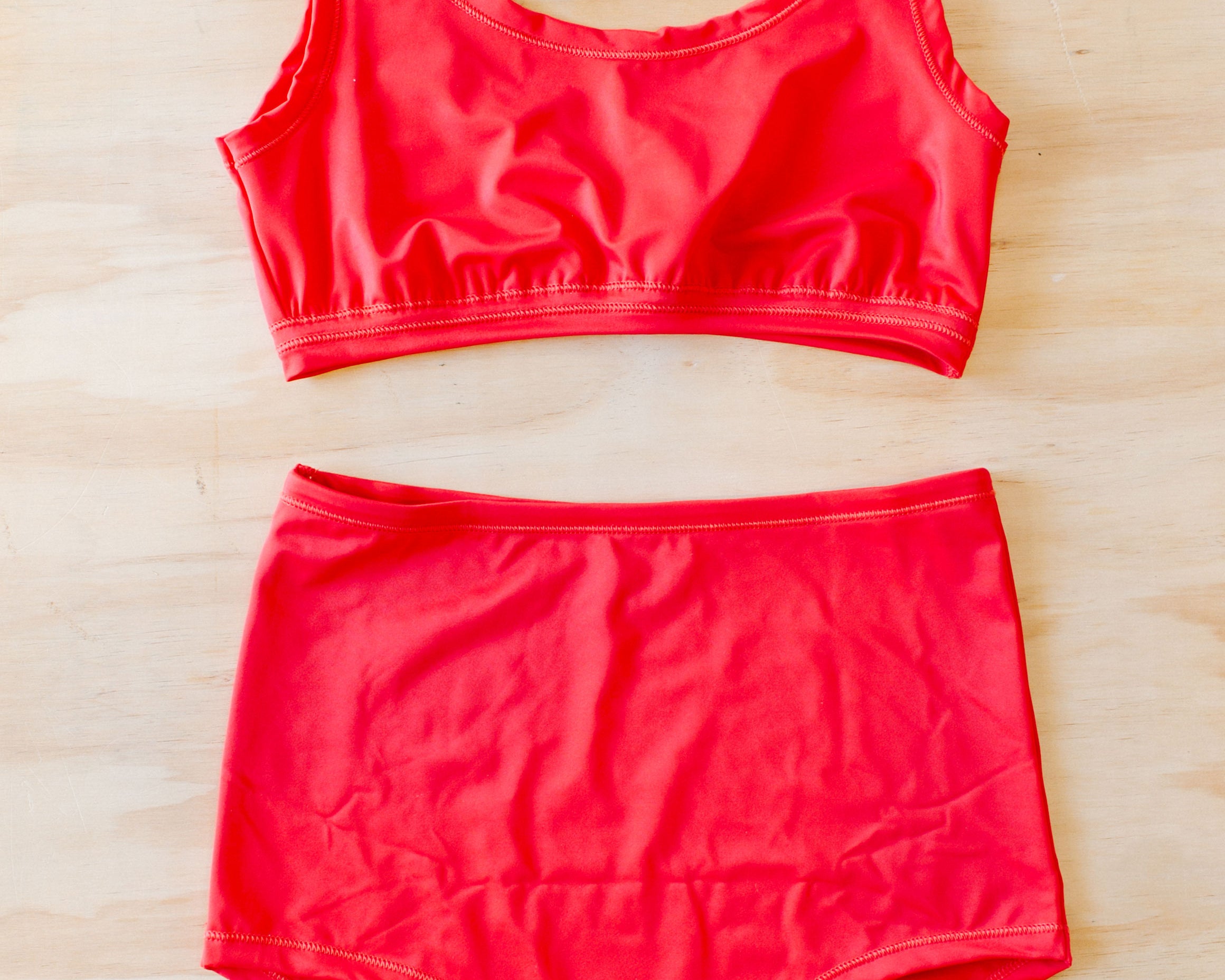 Flat lay on a wood surface of a Swimwear set with Sky Rise style bottoms in Classic Red.