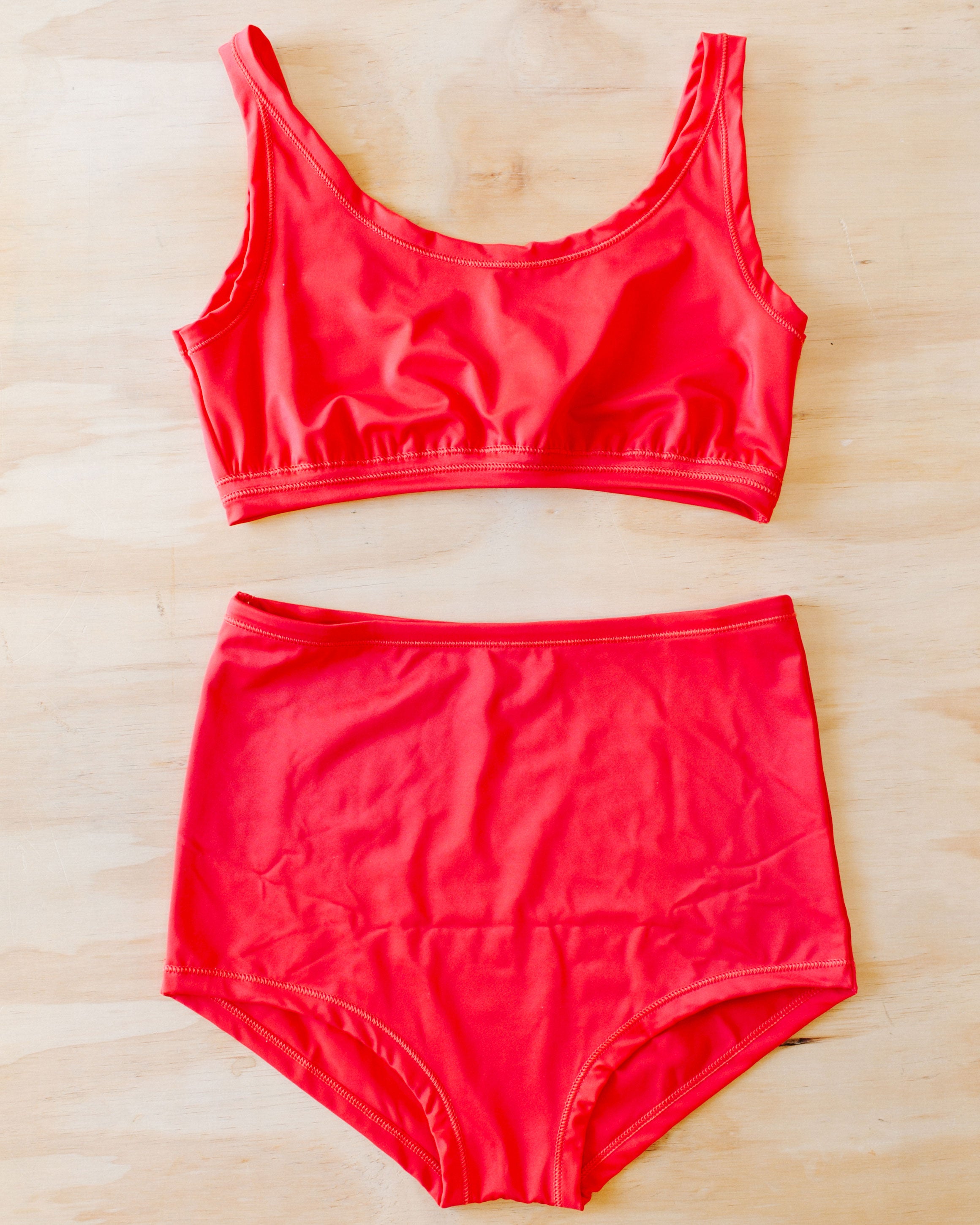 Flat lay on a wood surface of a Swimwear set with Sky Rise style bottoms in Classic Red.