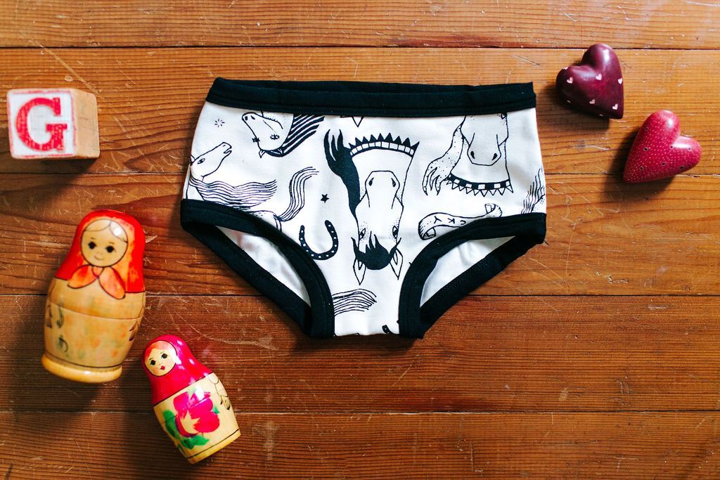 Horses in black and white on a brief style kid's underwear with toys laying around it.