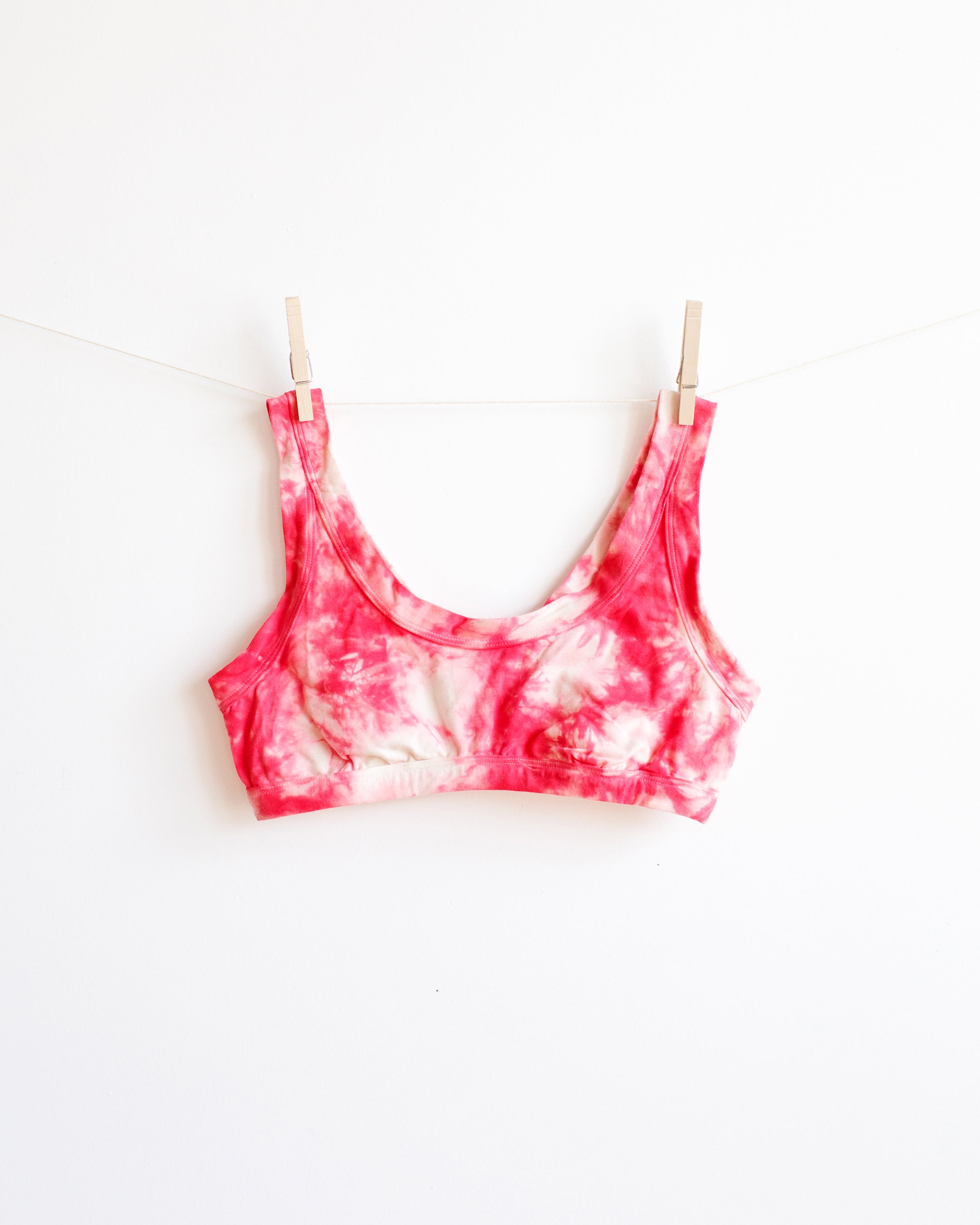 A Thunderpants Bralette with red and white scrunch dye hanging on a white backdrop.