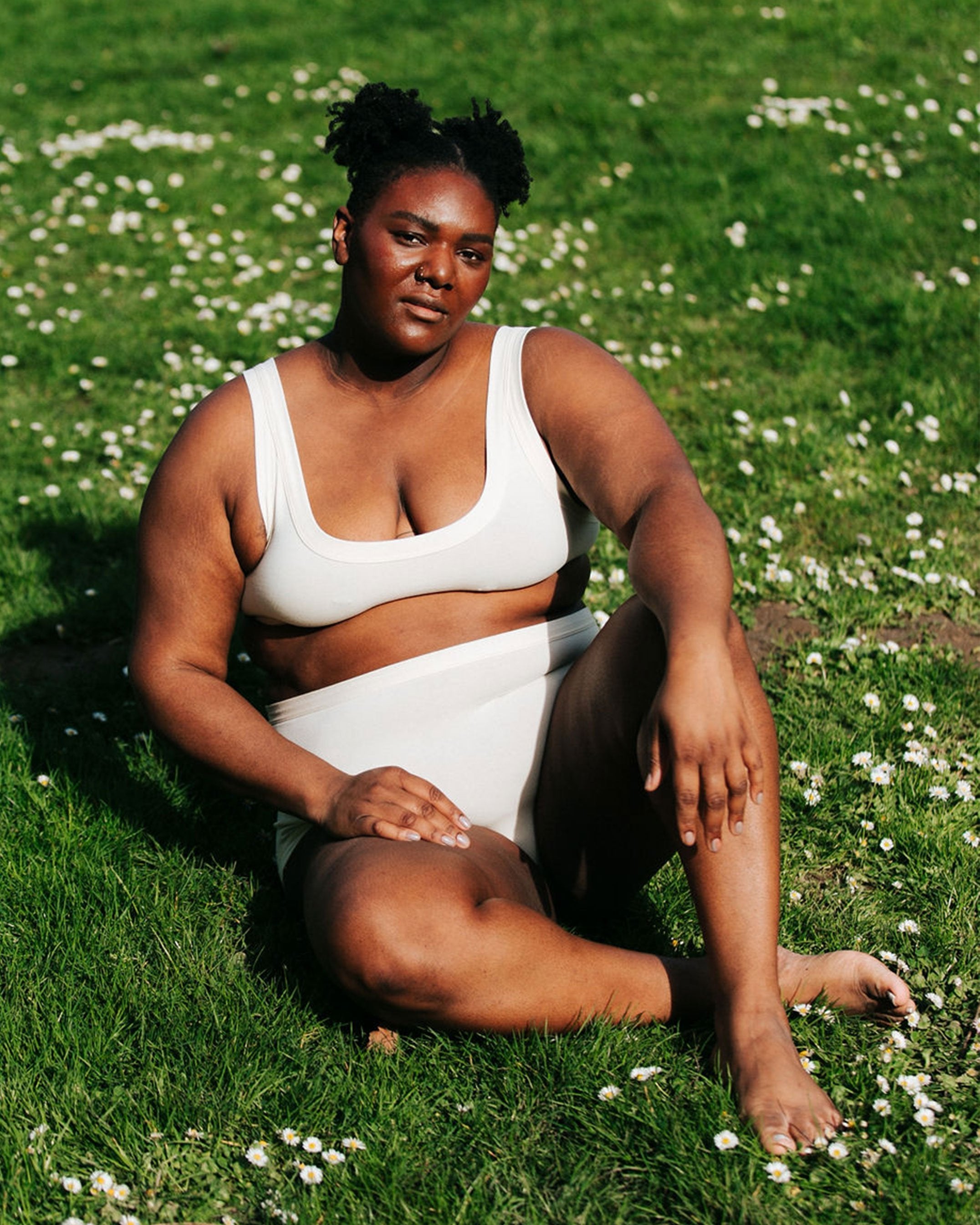 Plus-sized model sitting in the grass wearing Thunderpants organic cotton Bralette and Original style underwear in plain off-white.