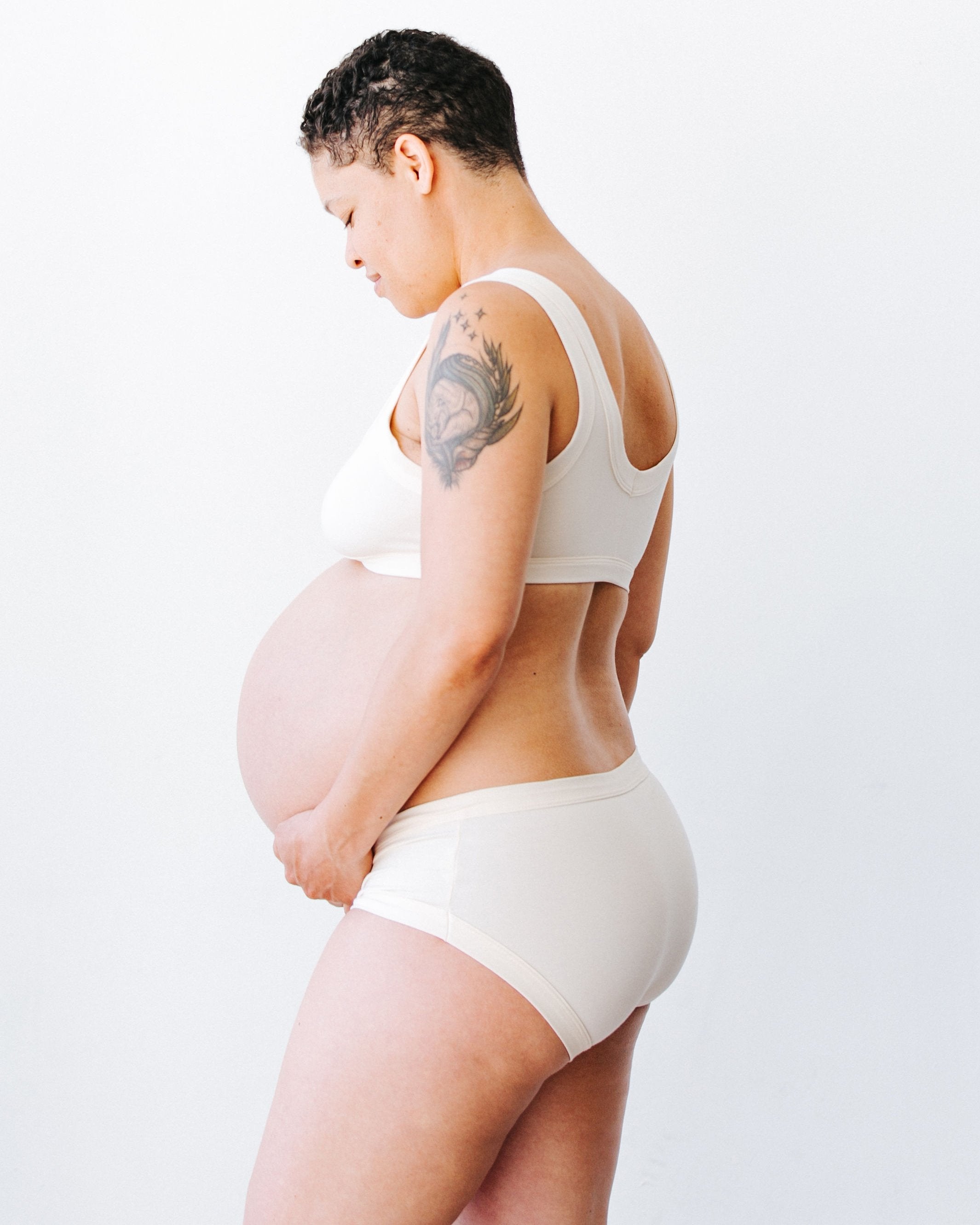 Beautiful pregnant model facing away wearing Thunderpants organic cotton Hipster style underwear and Bralette in plain off-white vanilla.