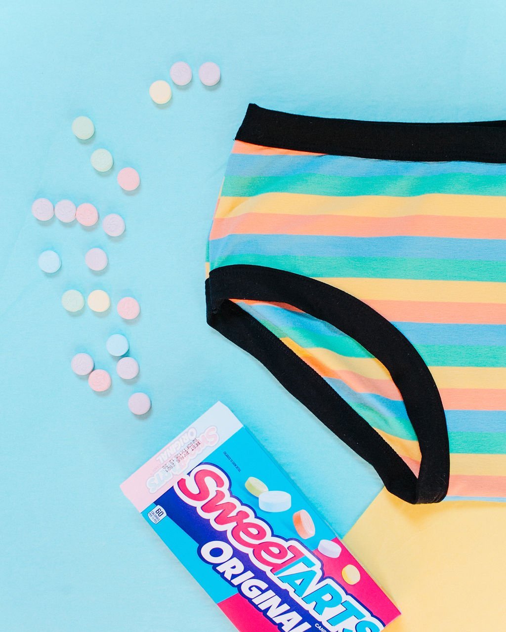 Flat lay of Thunderpants organic cotton Hipster style underwear in pastel stripes with a bright blue and yellow background and SweetTarts candy.