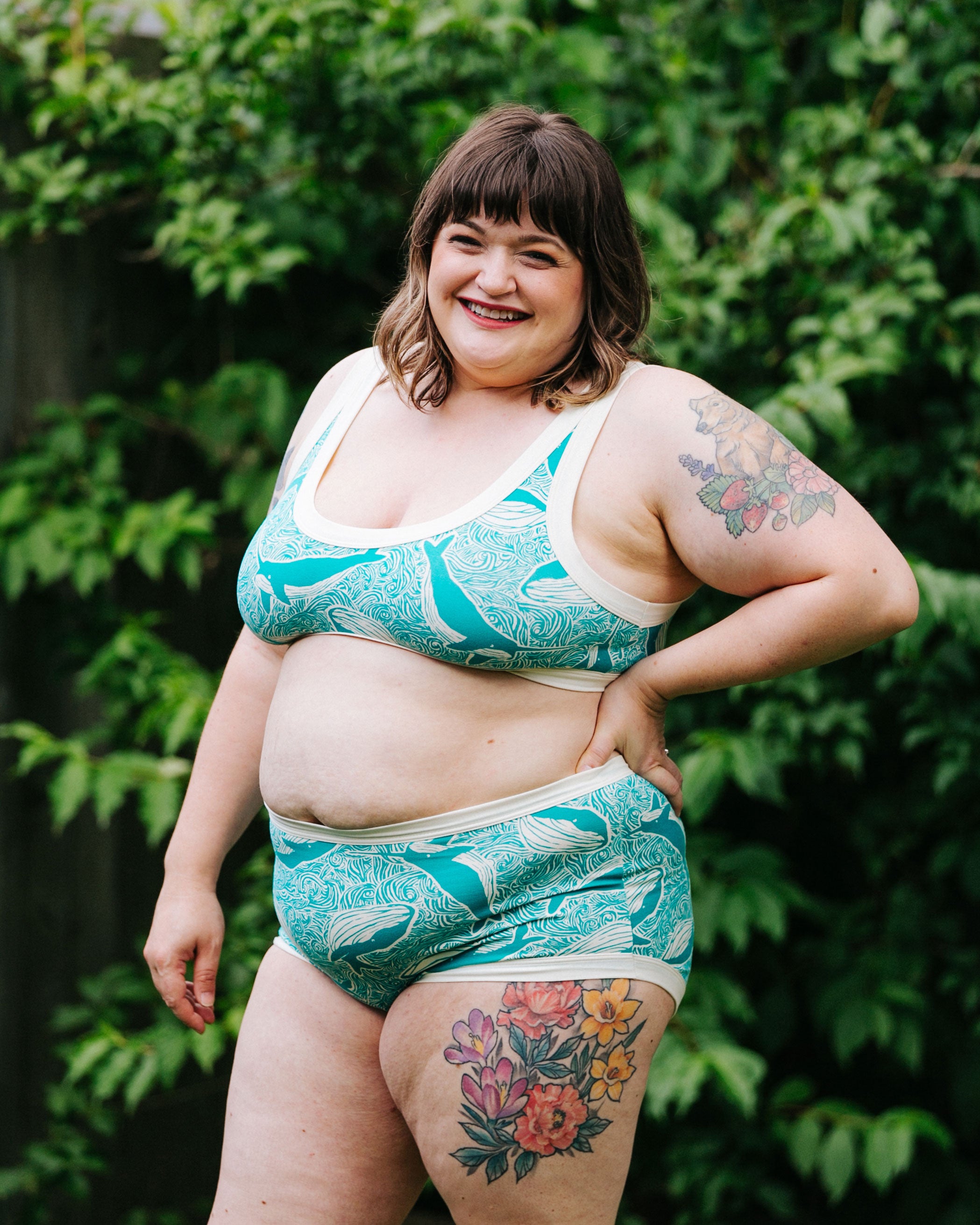 Model standing outside smiling wearing Thunderpants Organic Cotton Bralette and Original style underwear in our Marine Whales print: Turquoise all-over whale and ocean print.