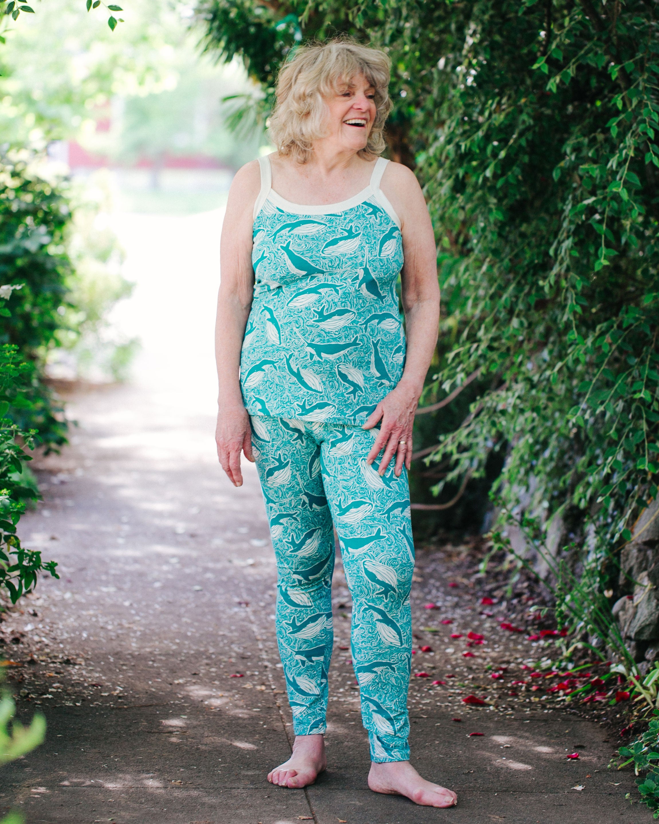 Older aged model smiling outside wearing Thunderpants organic cotton High Rise Leggings and Camisole in our Marine Whale print: turquoise whale and ocean all-over print.